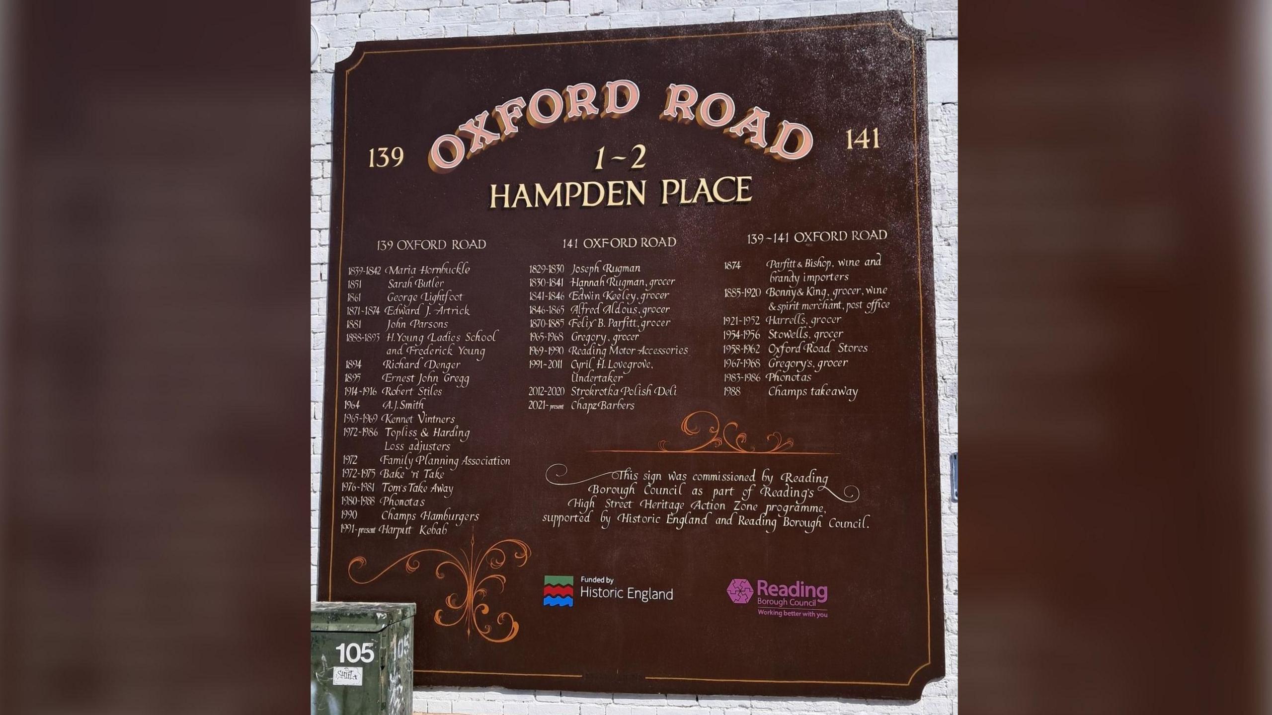 A dark red sign painted on to a brick wall which lists a number of former businesses with the dates that they operated out of 139 - 141 Oxford Road.