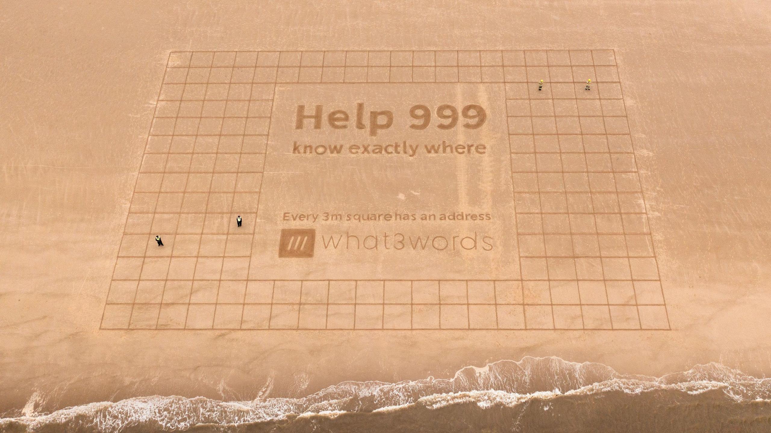 A large piece of sand art showing a grid of more than 100 boxes measuring 3m square. In a large central box there is lettering reading Help 999 know exactly where - Every 3m square has an address' and the What3Words logo.