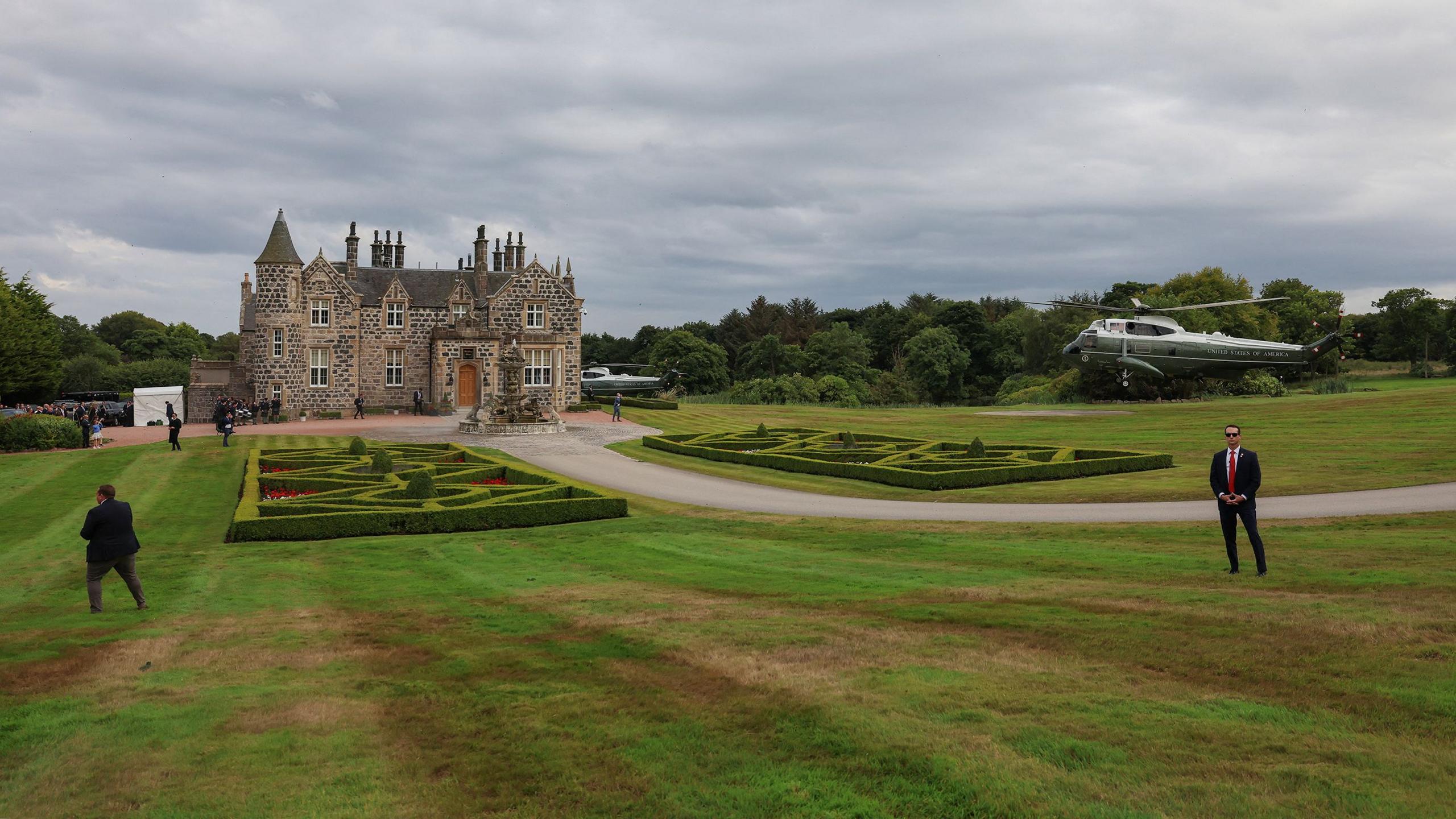 Two helicopters land around a small castle building in the middle fo a golf course
