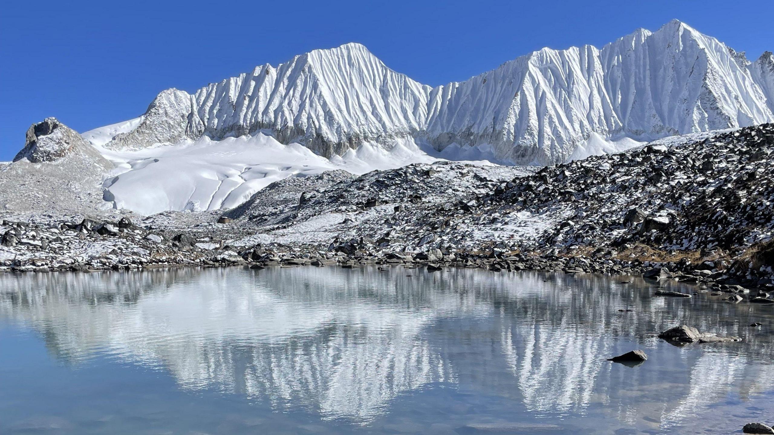 Snow-covered mountains reflected in a lake on a clear, sunny day in Bhutan