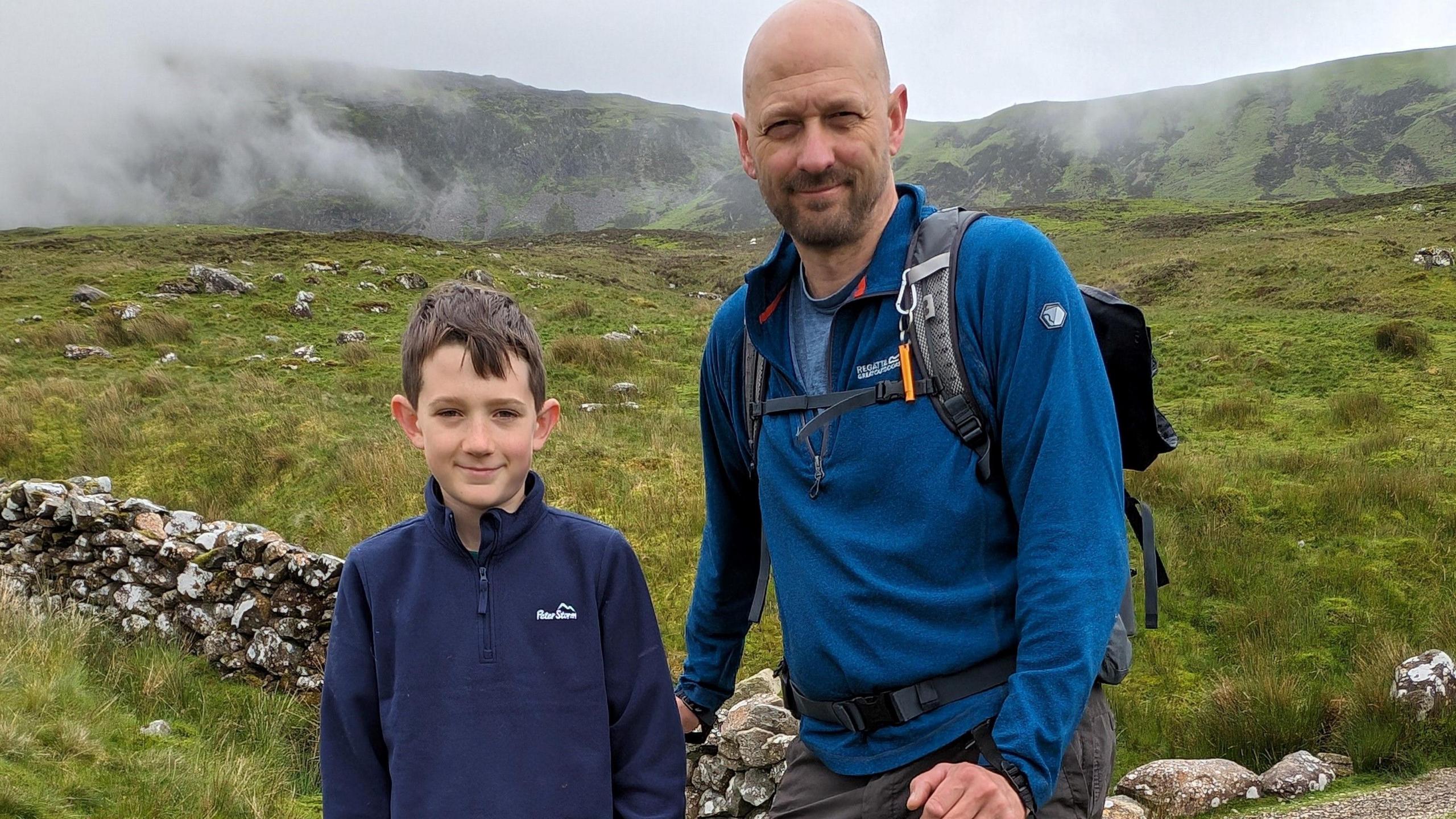 A young boy standing next to his dad on a mountain