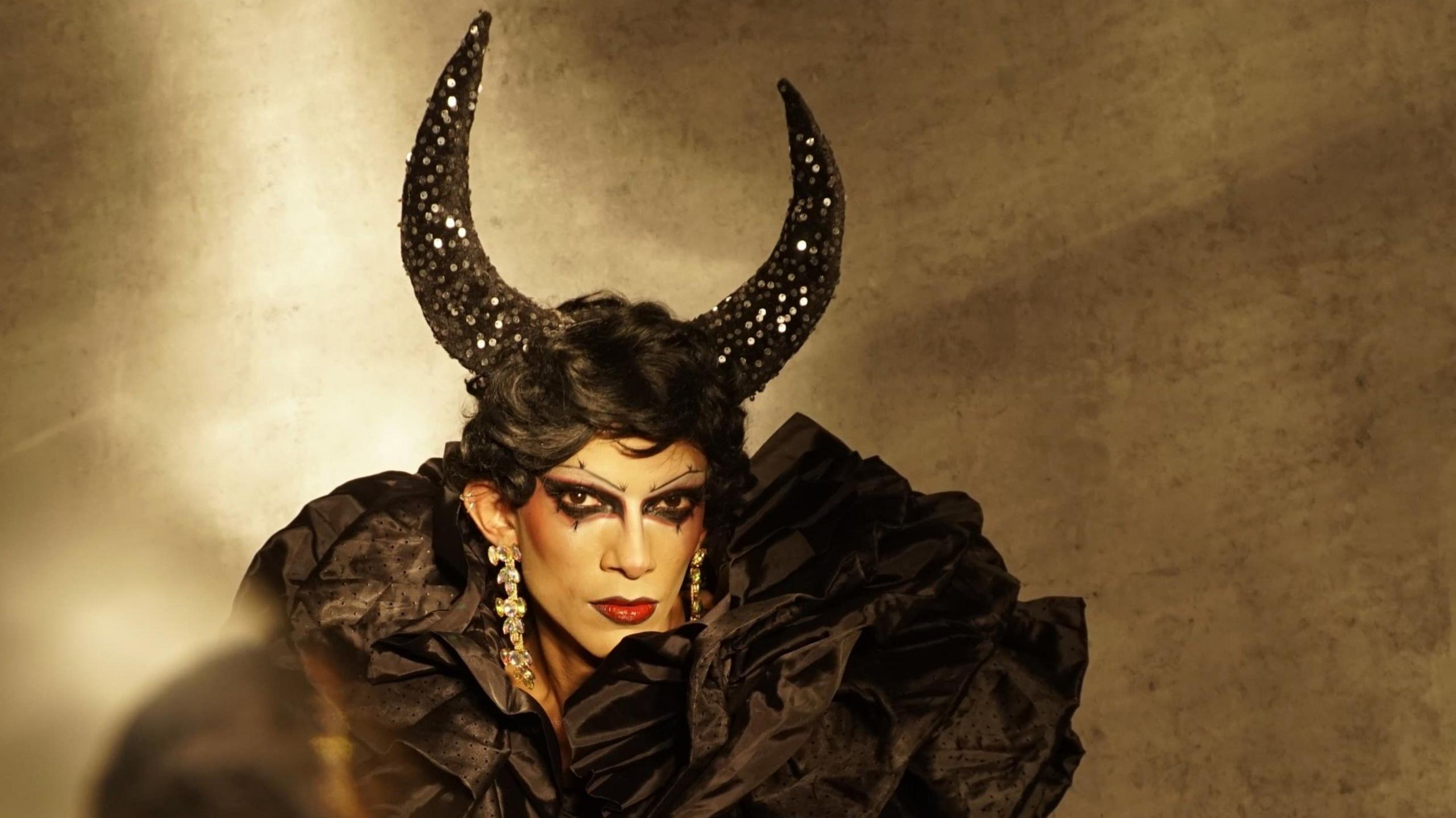 Zeeshan Ali in drag, wearing black horns and a short black wig