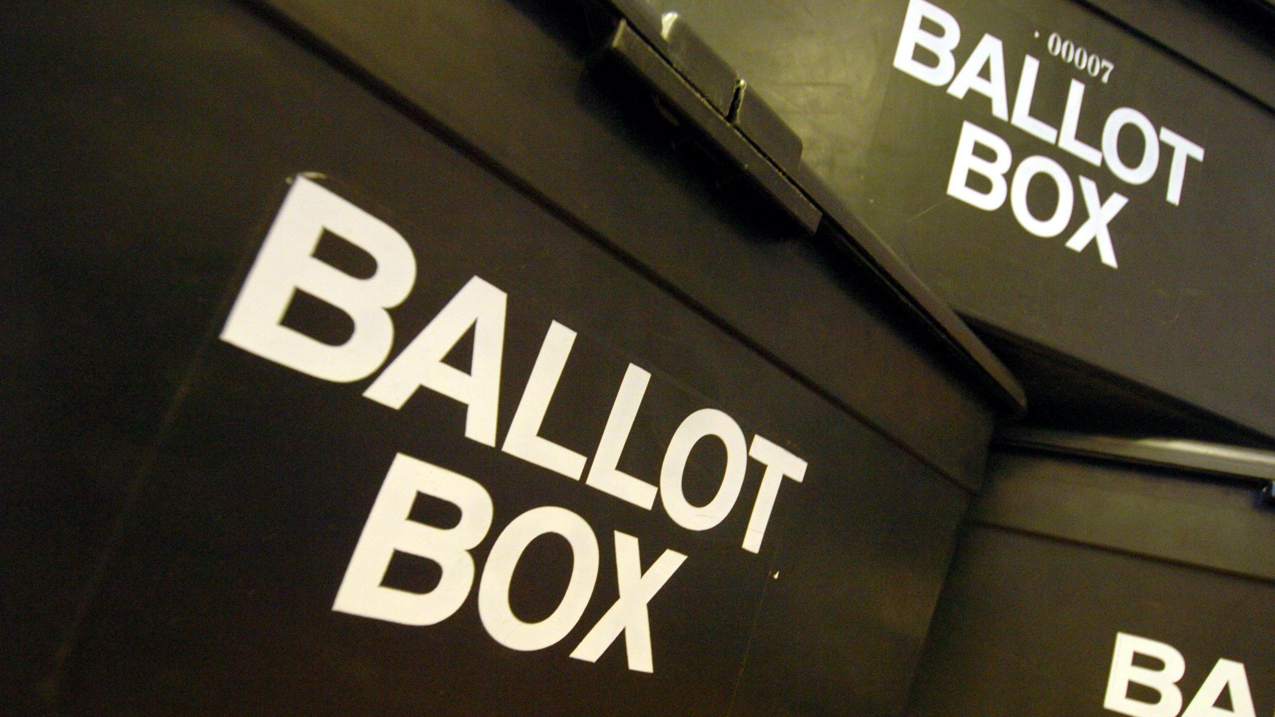 A stock image of three black ballot boxes stacked on top of each other, they all have the words ballot box written on them in white capital letters