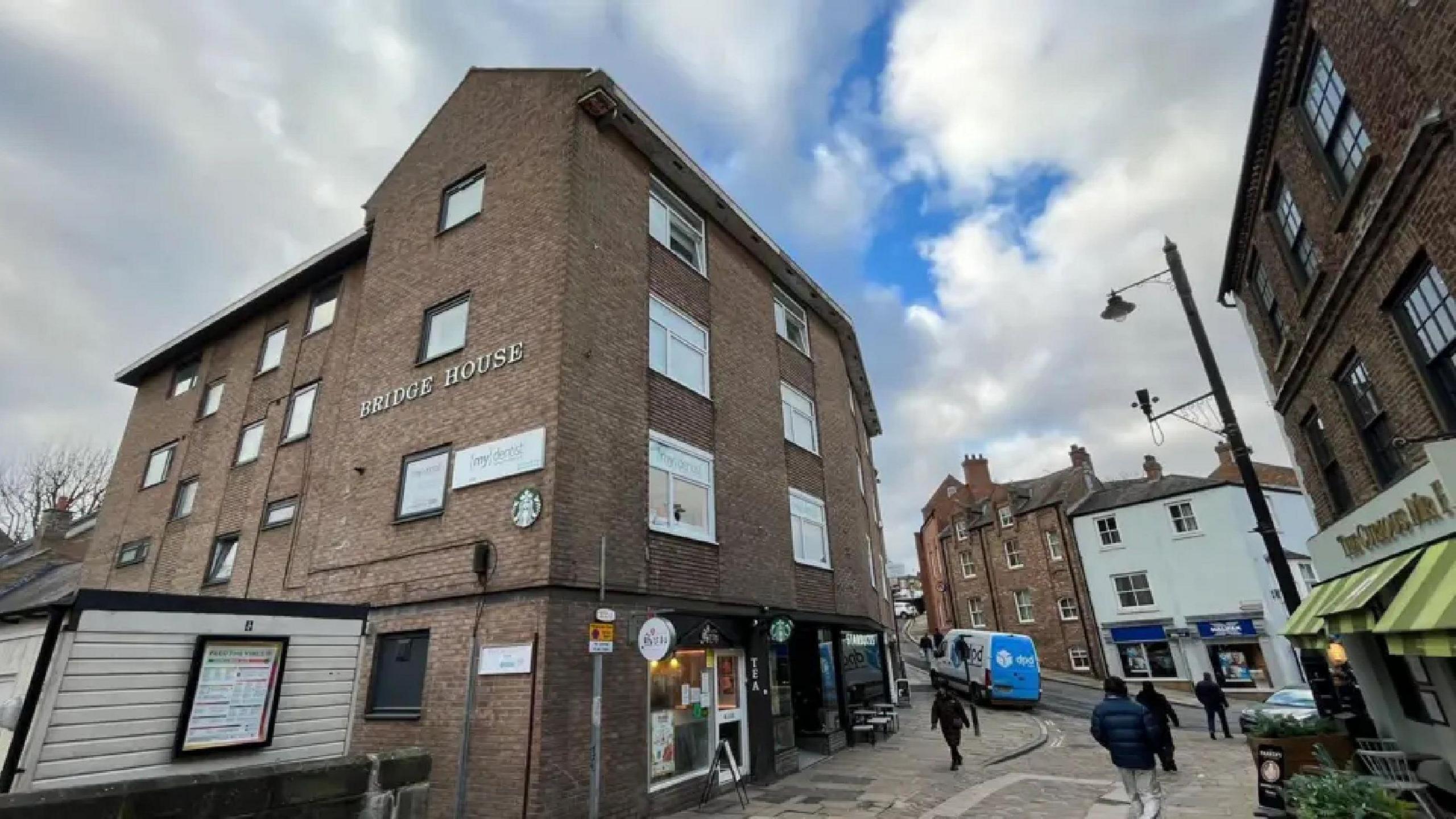 Bridge House, a brick building with signs for Mydentist on the first floor. A number of people are walking along the pavements at the front of the building and a white-and-blue DPD delivery van is parked nearby.