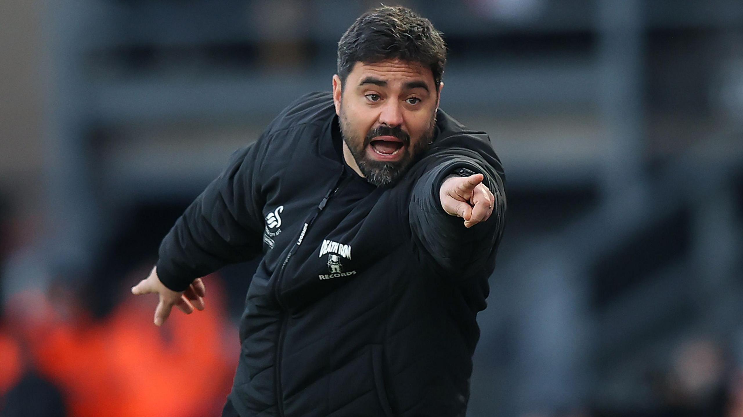 Vitor Matos wearing black Swansea jacket points towards camera