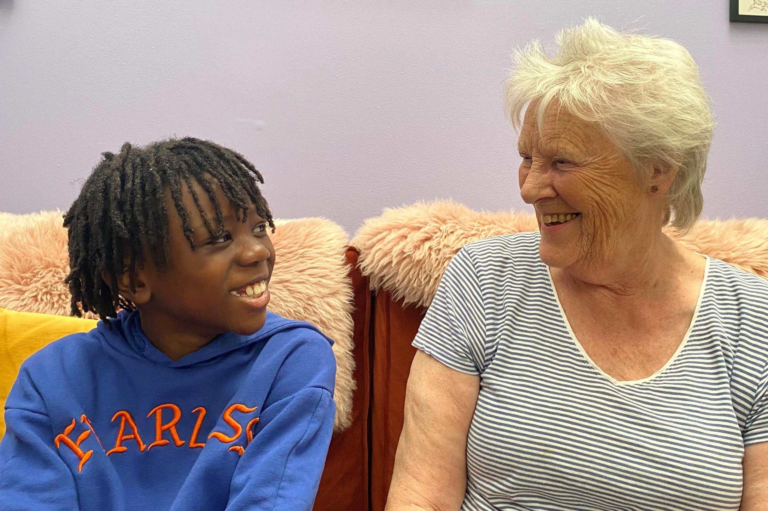 Smiling young black boy with dark hair sits beside smiling older white woman with grey hair