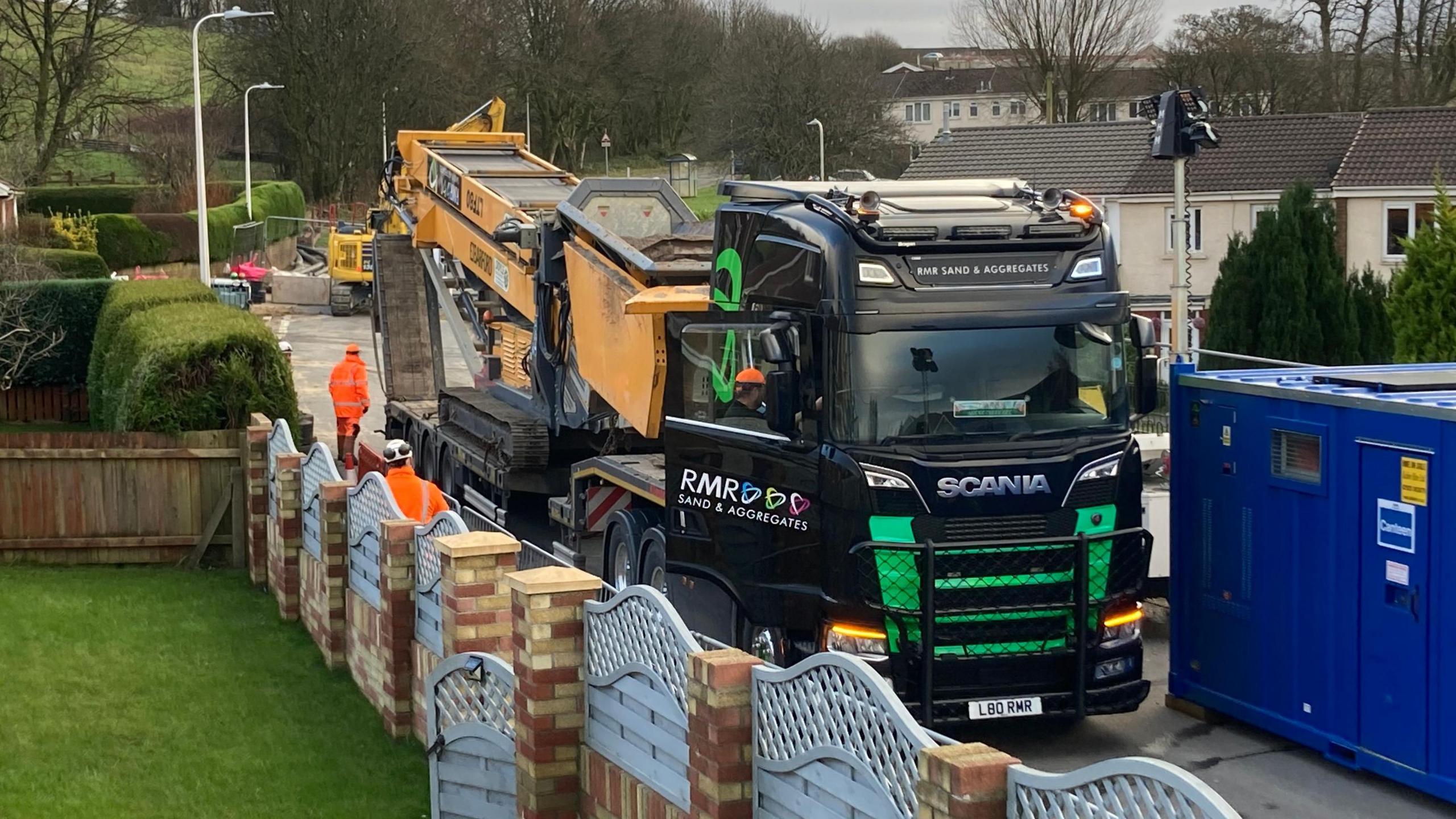 A conveyor lorry is parked on a residential street next to the sinkhole. 