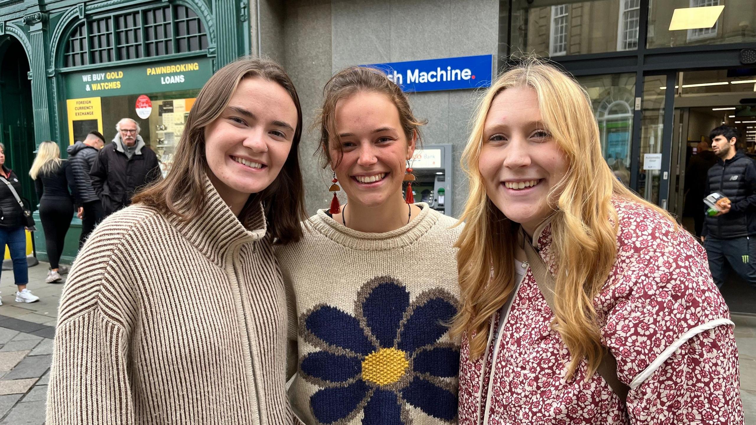 Durham University students Hannah Cathcart (left), Caragh Puttick (centre) and Lydia Campbell outside Whittard Of Chelsea Durham, 14 Market Place, City of Durham. They are standing in a street smiling broadly.