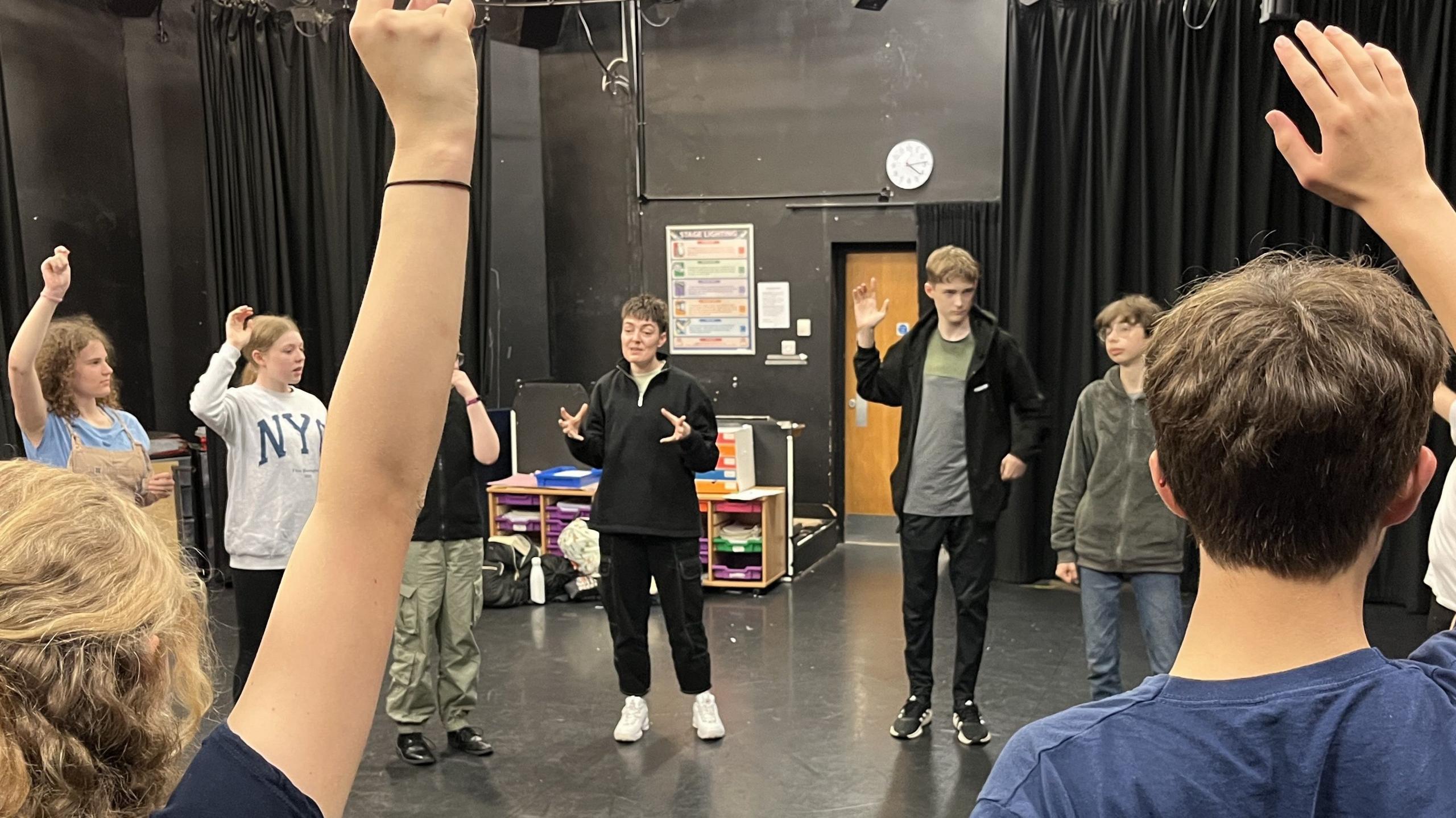 Teenagers taking part in the workshop stood in a circle with their hands raise