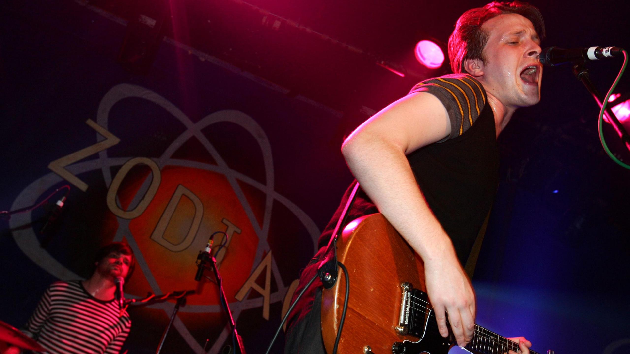 Barry Hyde on stage in Oxford in 2006. He is wearing a T-shirt and is playing a guitar and singing into a microphone with his eyes closed.