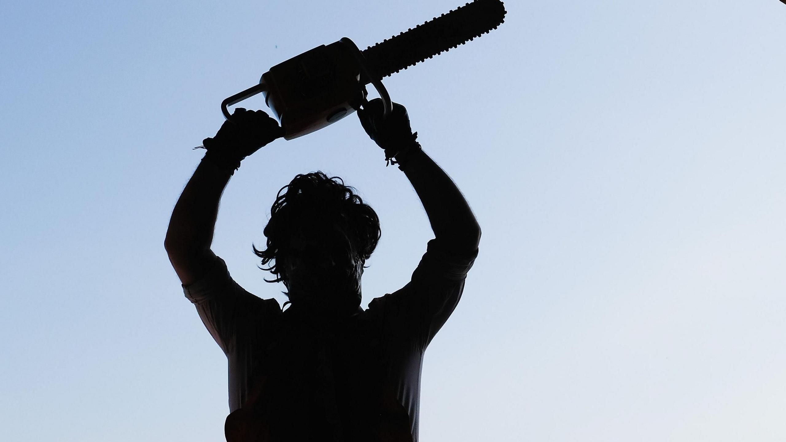 A silhouetted image of somebody dressed as Leatherface holding a chainsaw above their head