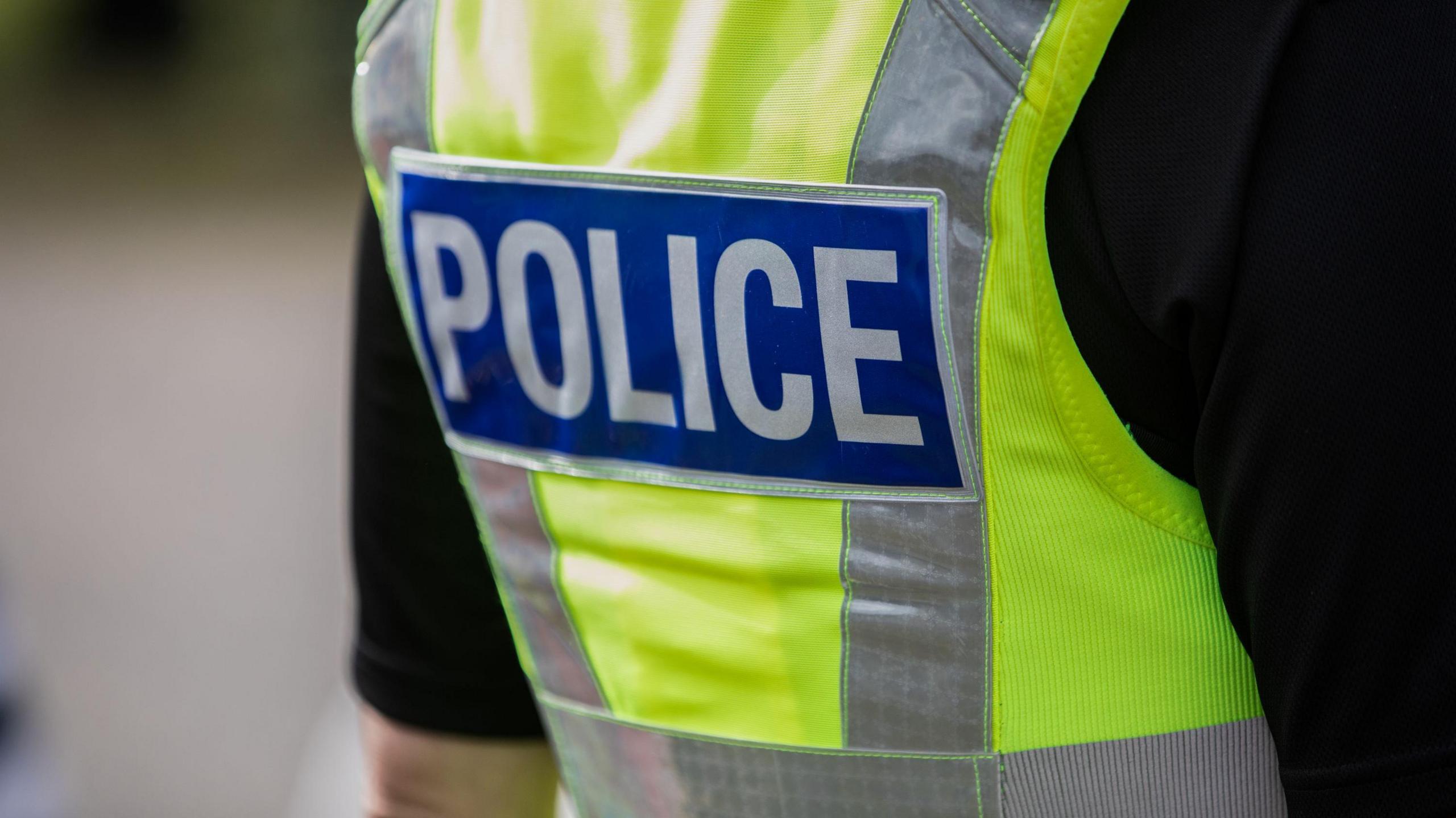 A police officer wearing a hi-vis vert, photographed from behind. You can only see their torso.