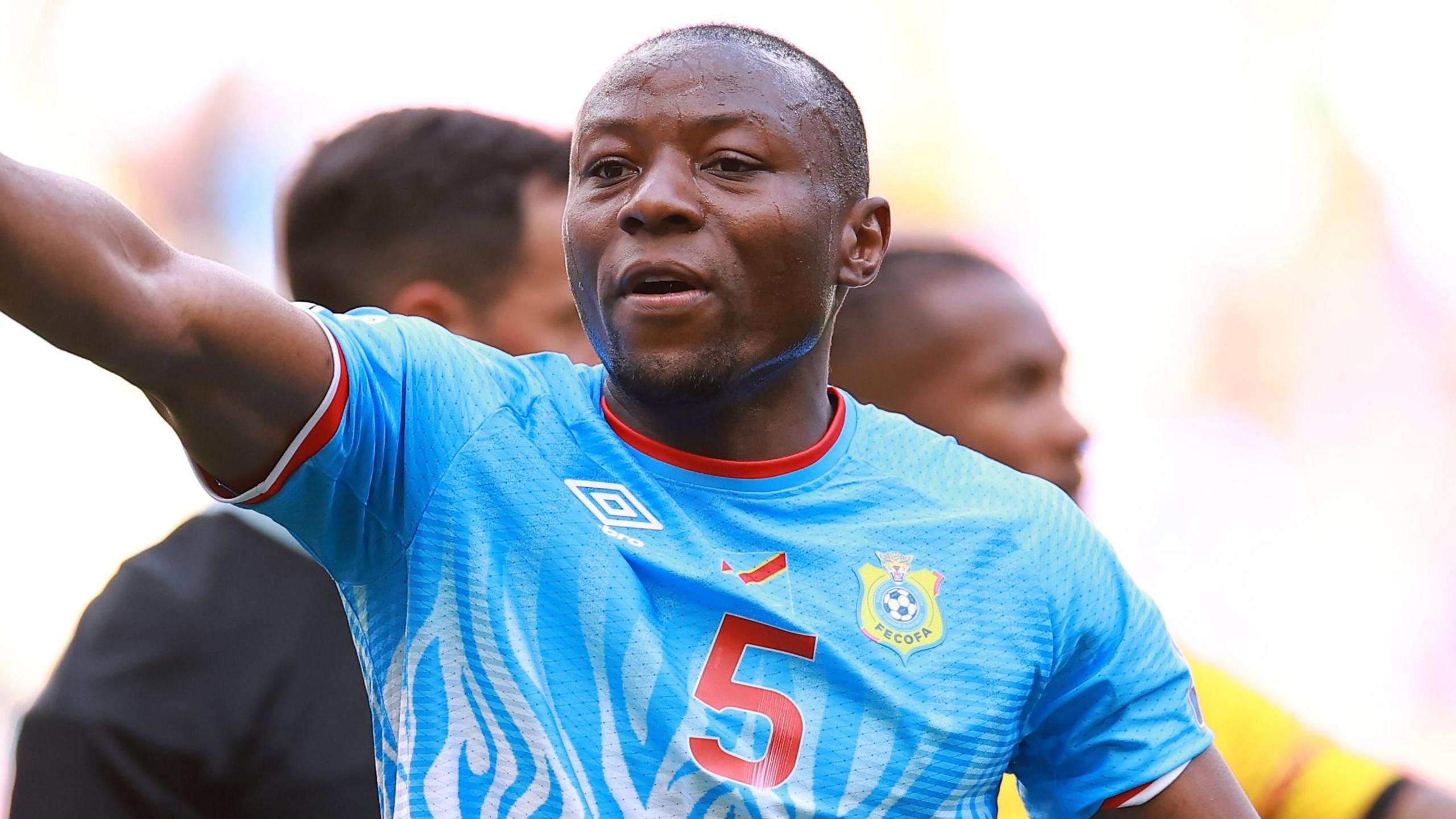 Edo Kayembe points to his right while wearing DR Congo's light blue shirt.