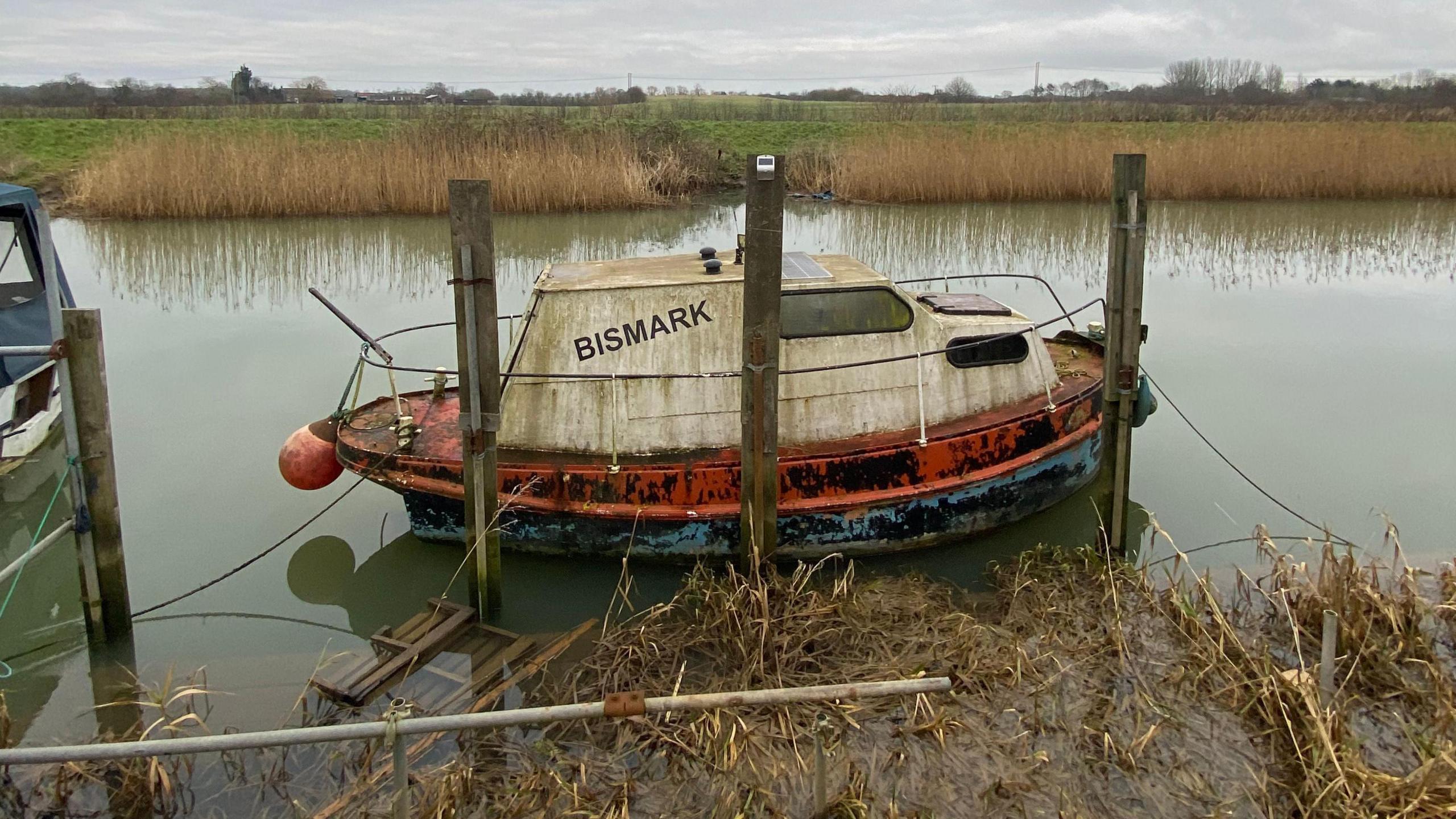 An old boat tied up to the riverbank surrounded by overgrown weeds