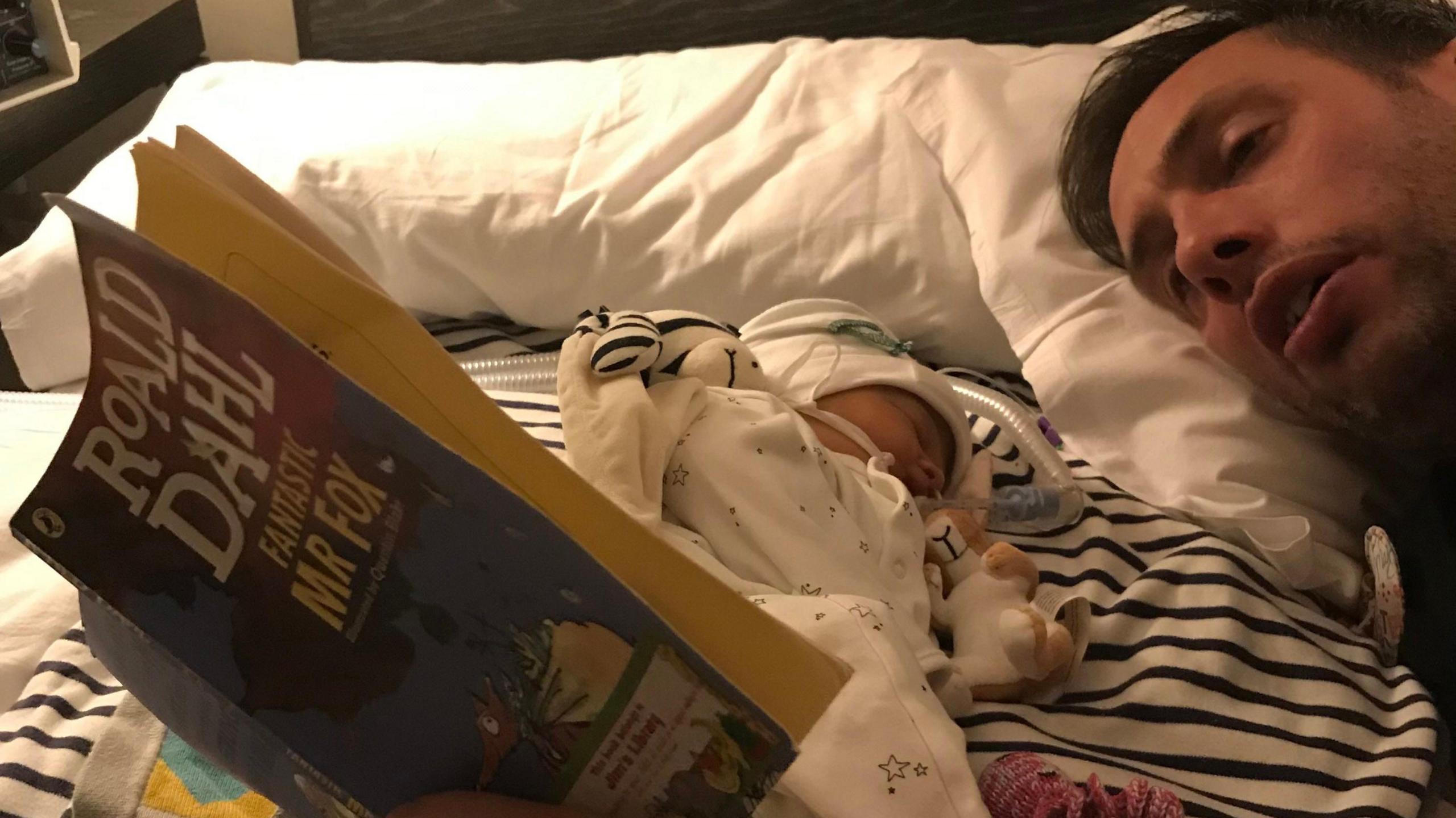 Ryan Lock laying beside Ida in bed reading a Roald Dahl book.