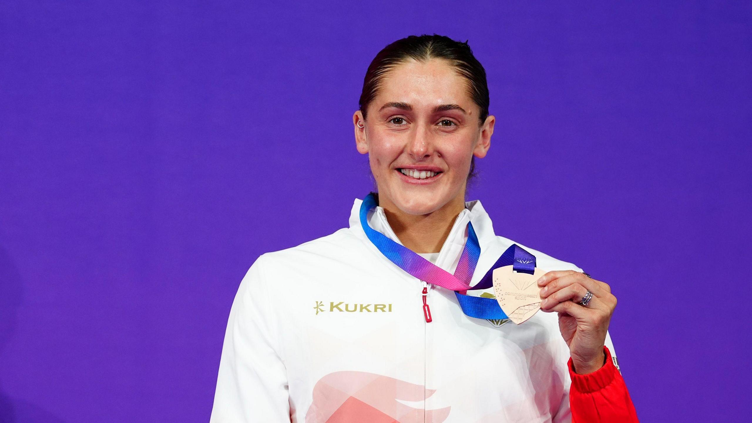 Imogen Clark holds up her bronze medal in front of a purple background at the Commonwealth Games in Glasgow
