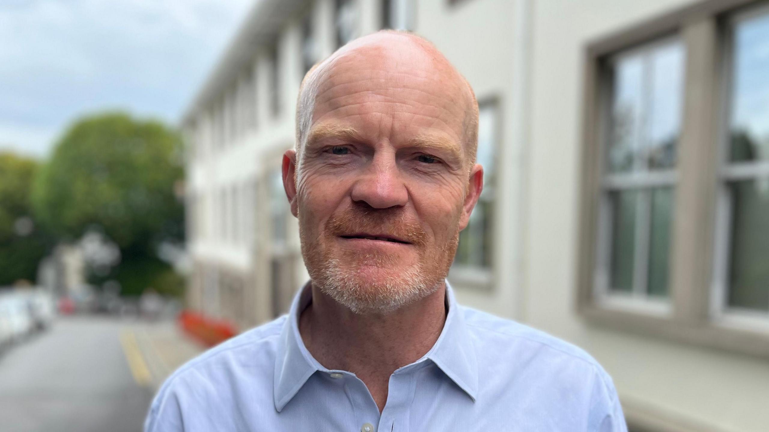 Deputy Gavin St Pier: a bald man with a grey and ginger beard. He is wearing a blue shirt. 