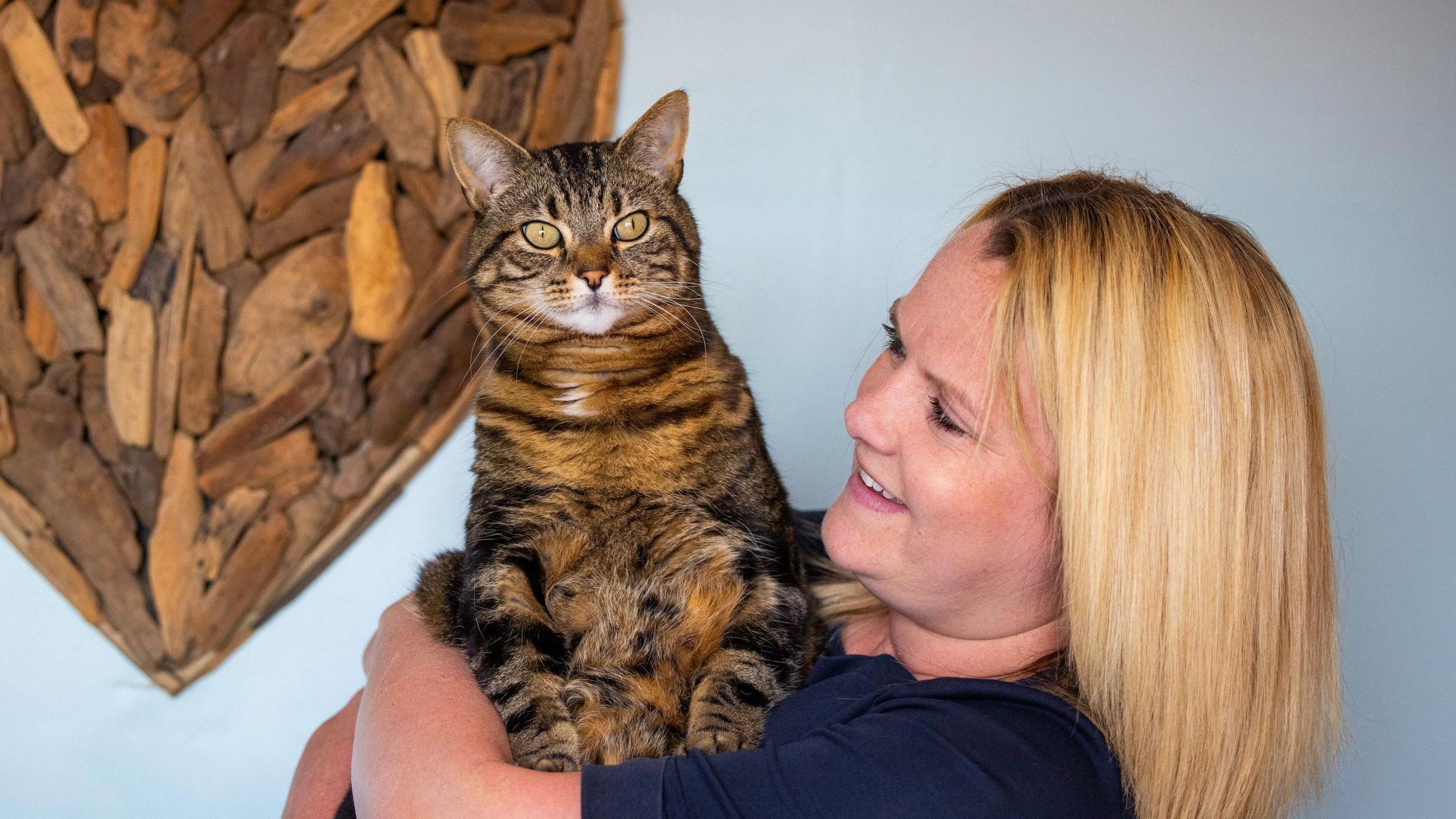 A woman cuddling a chunky cat, which frankly looks a little disinterested