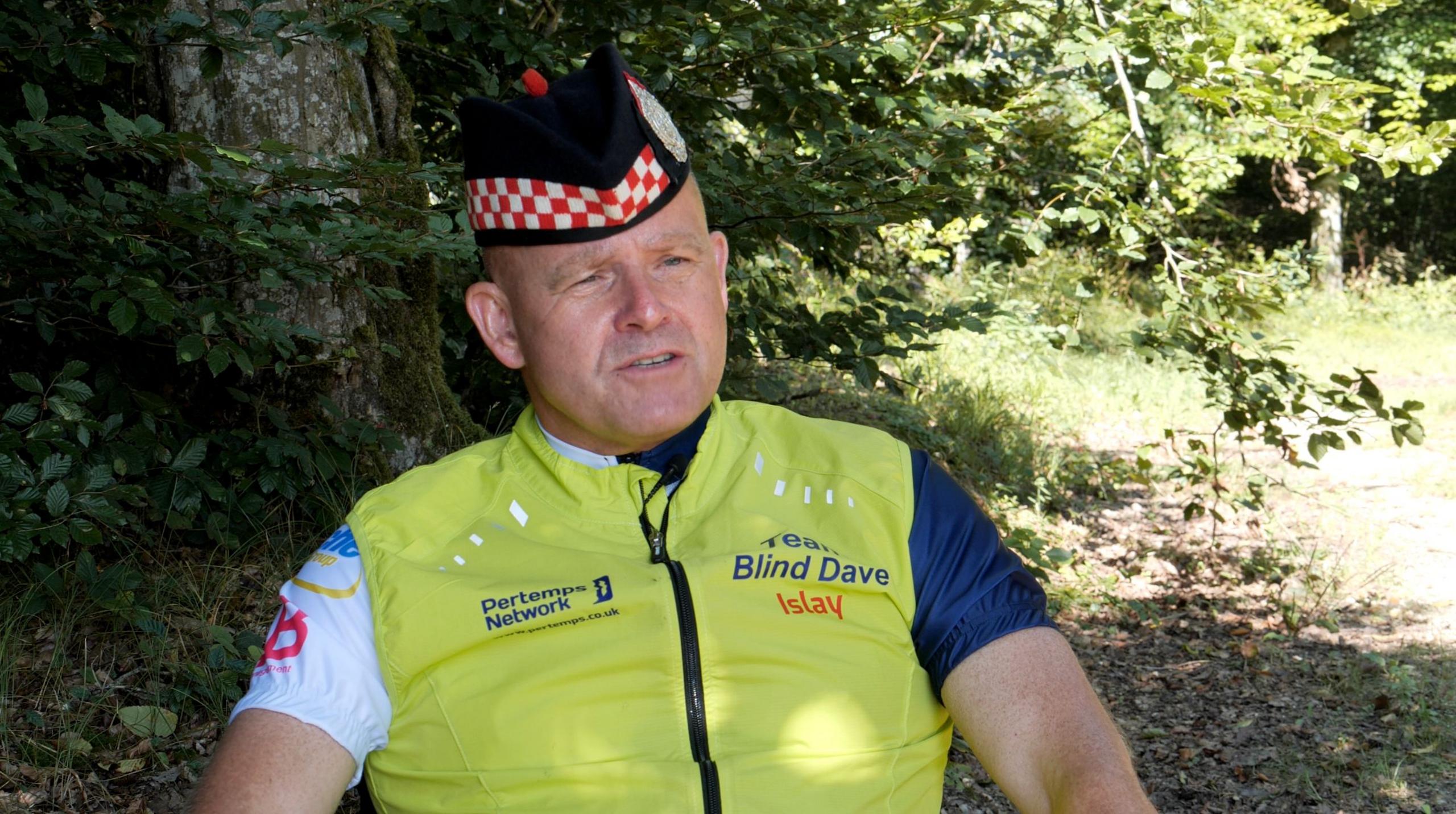 Seated man with an army beret on and lime green gilet with Team Blind Dave emblazoned on it