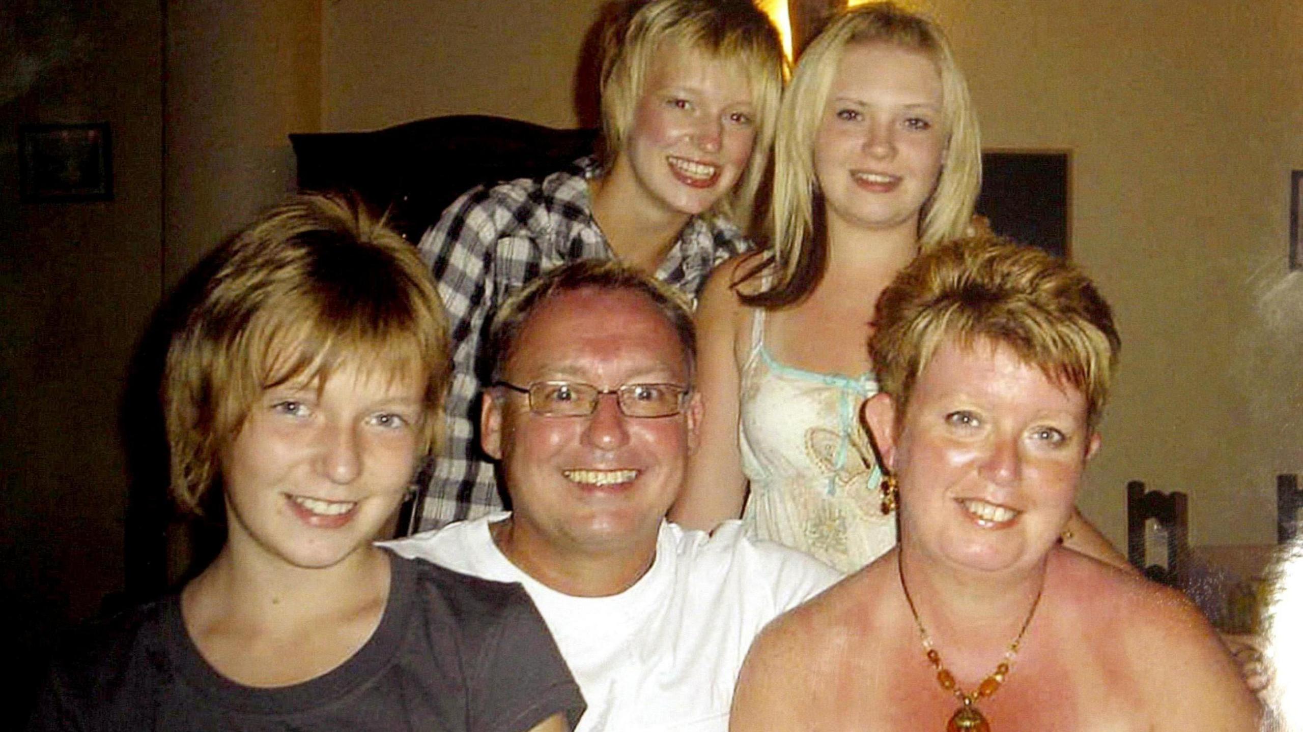 A family of five people, a man, woman and their three daughters, all smiling.