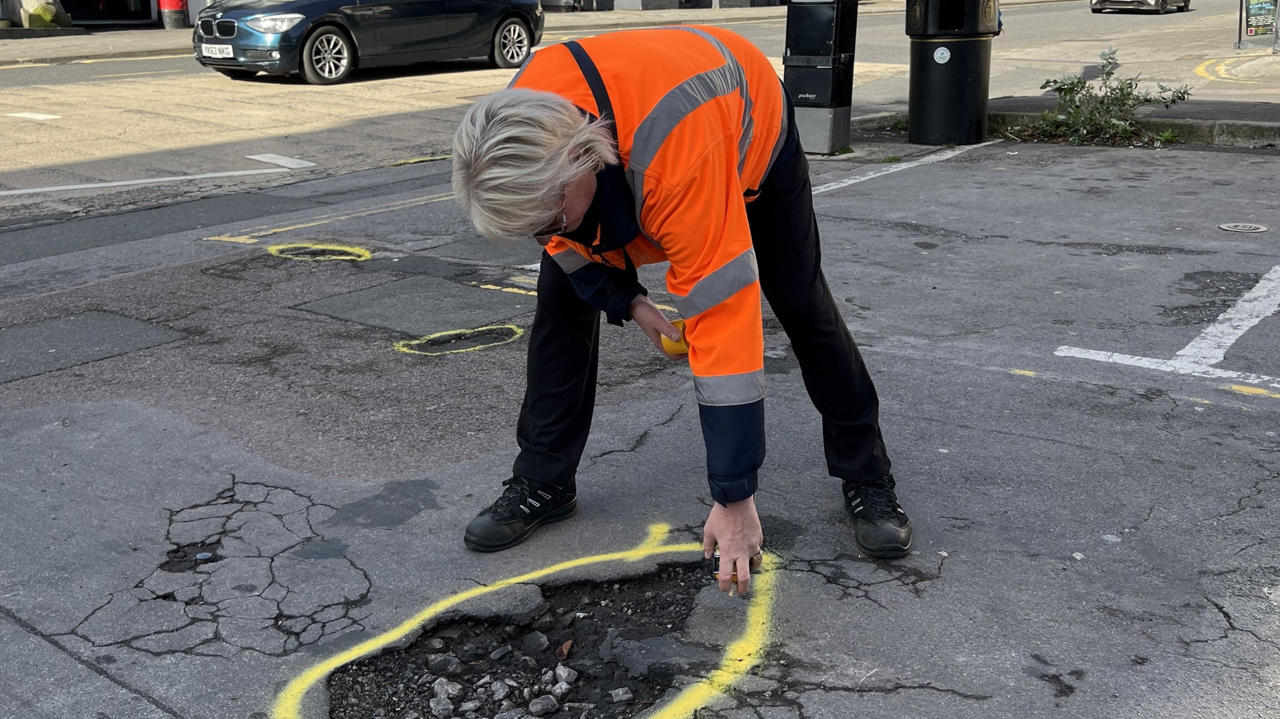 Highways Inspector, Marcia Belcher, circling a pothole will yellow spray paint