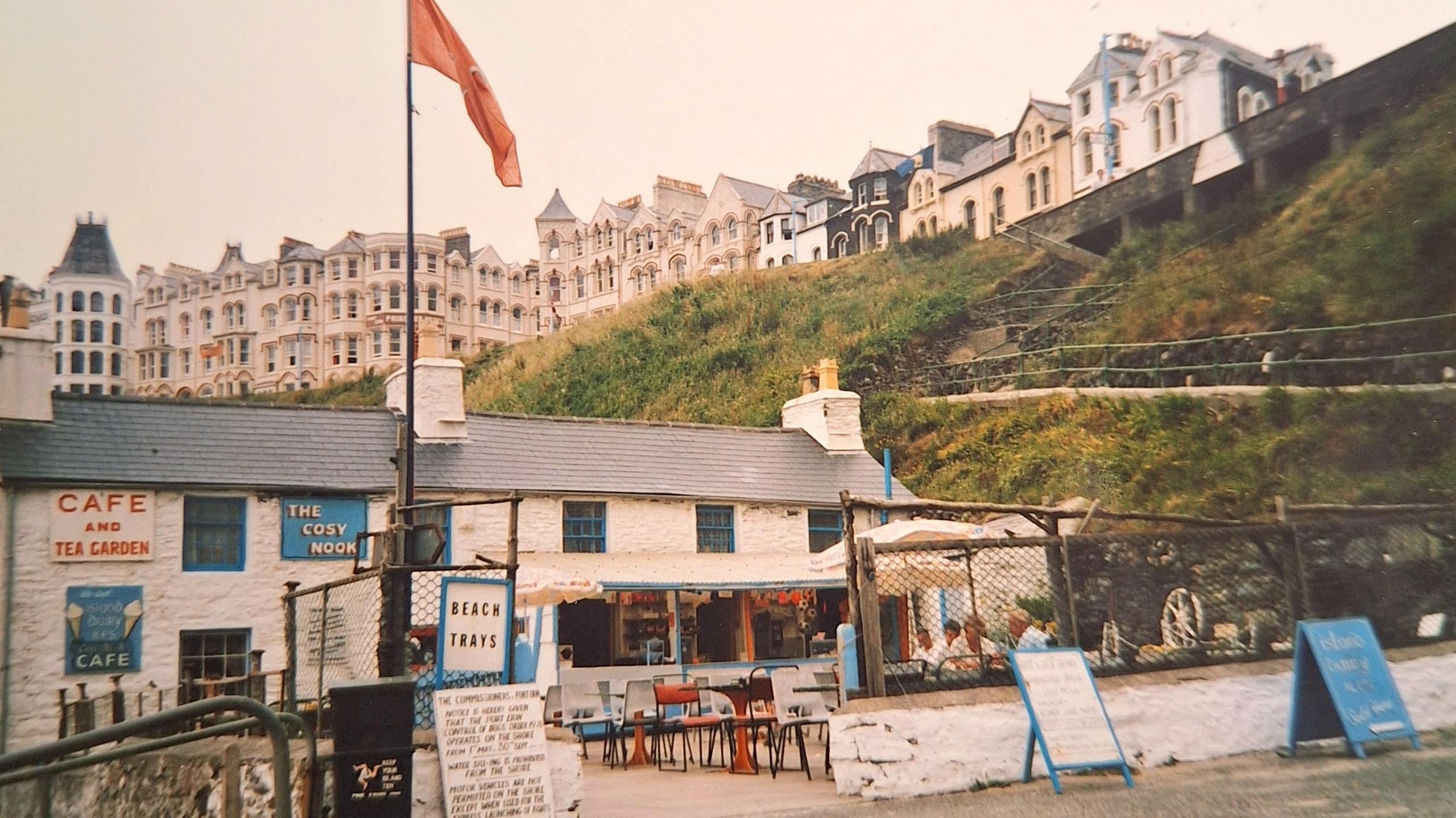 Photograph of the Cosy Nook from the 1990s. There are tables and chairs outside the small white cottage, as well as a counter.