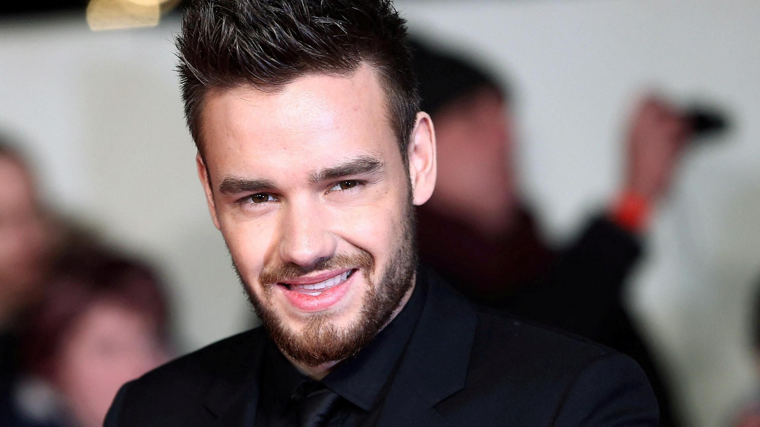 Singer Liam Payne, dressed in a black suit, shirt and tie, poses for photographers at a movie premiere.