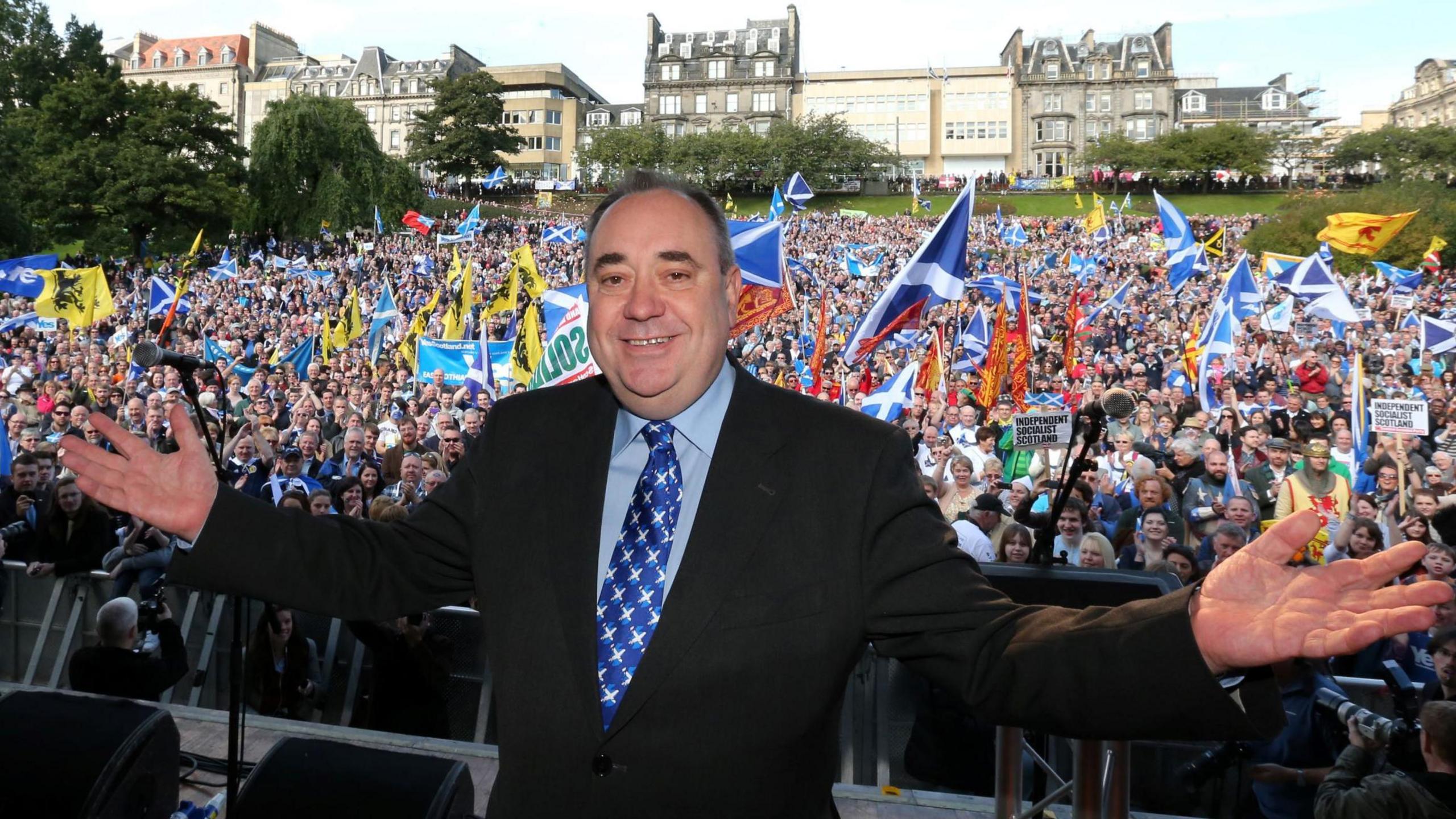 Alex Salmond at a rally for Scottish Independence in Princes Street Gardens, Edinburgh, in 2012. He is smiling at the camera with arms streached out - behind him are thousands of people waving flags and cheering