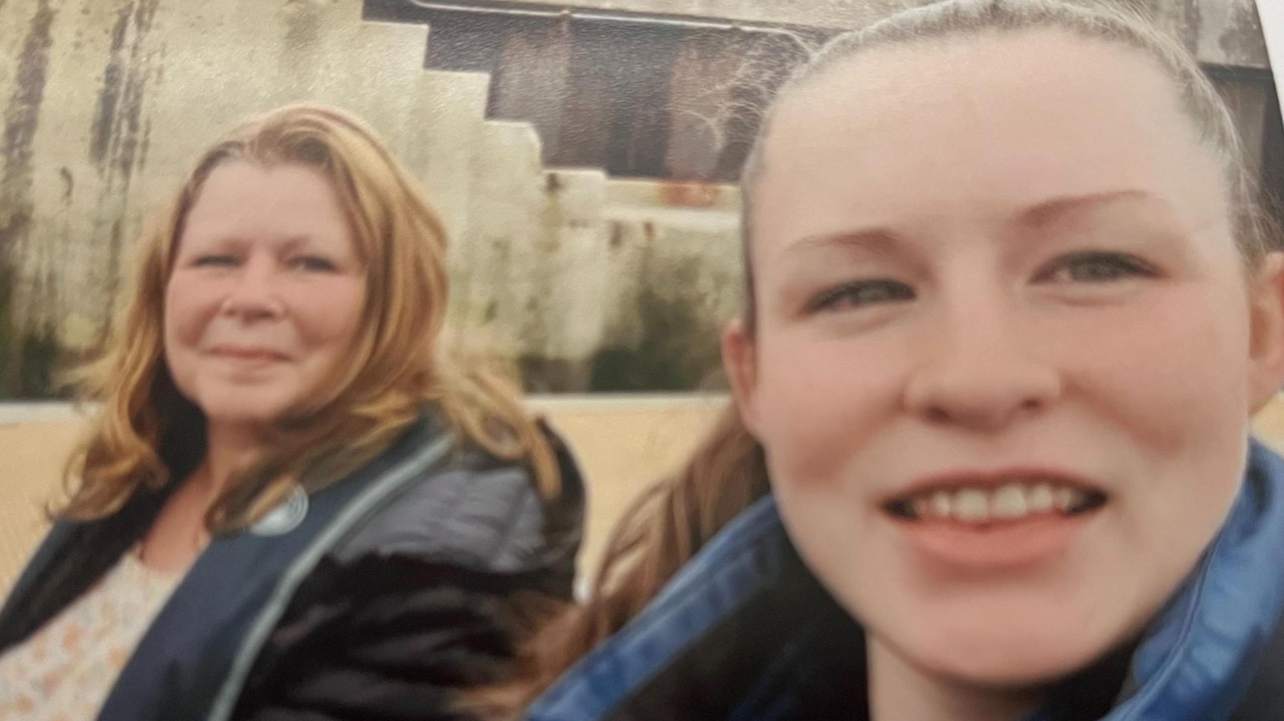 Teresa and Morgan both smiling and looking at the camera. Morgan is wearing a denim jacket and has a ponytail. Teresa has red shoulder-length hair. 