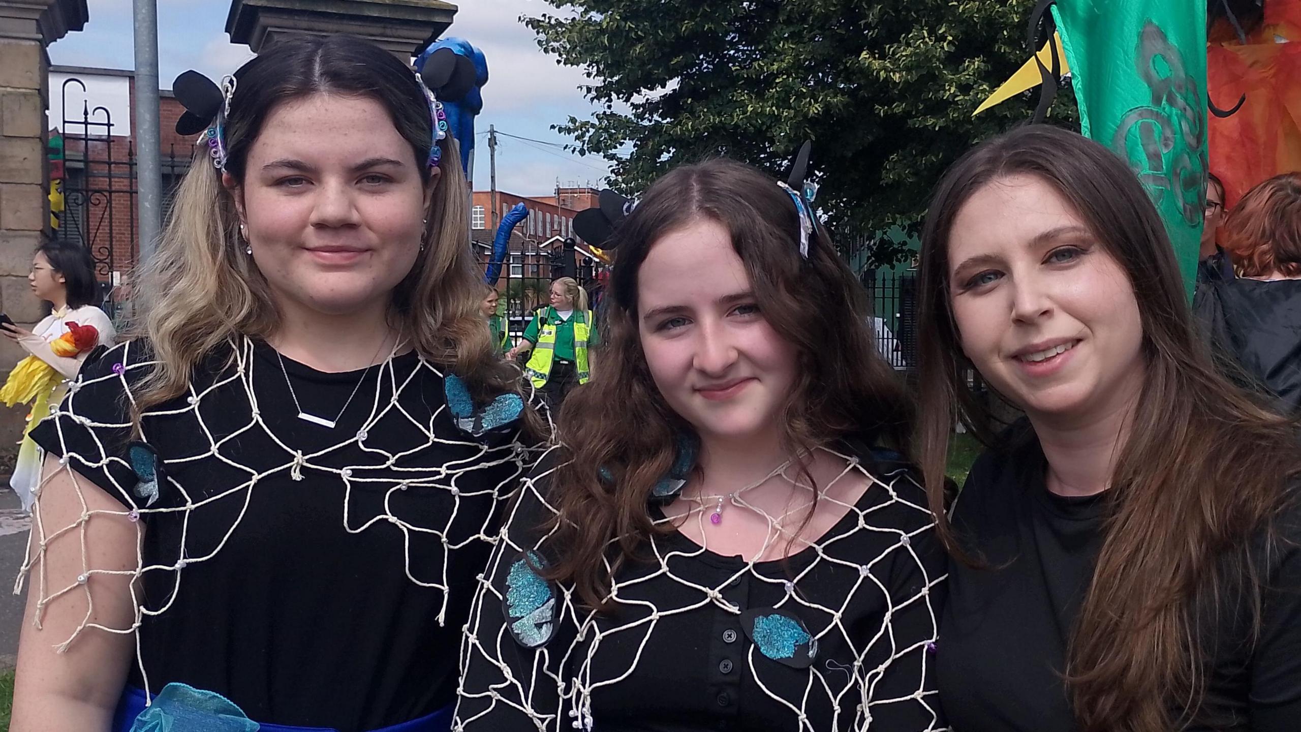 Three women smiling at the camera. All three are wearing black tops.