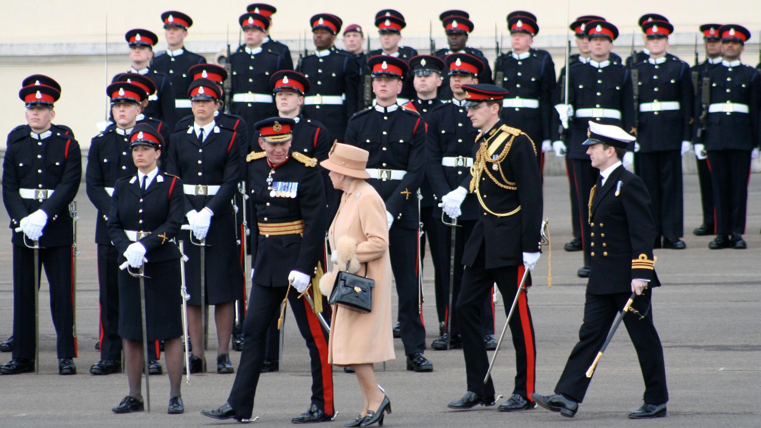 Queen Elizabeth II is inspecting troops in ceremonial uniform