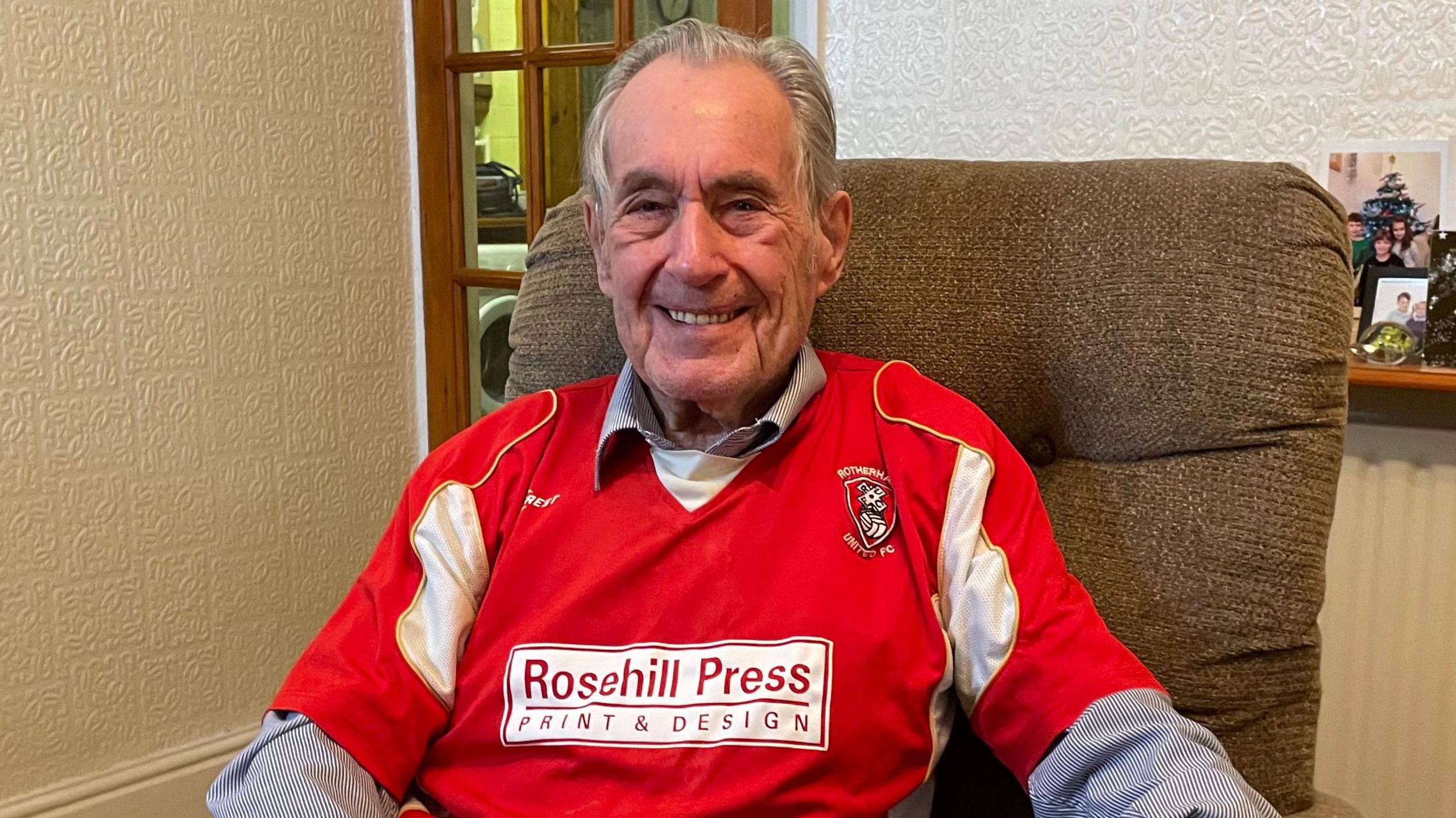 Dennis, an elderly man, smiling and wearing a Rotherham United shirt.