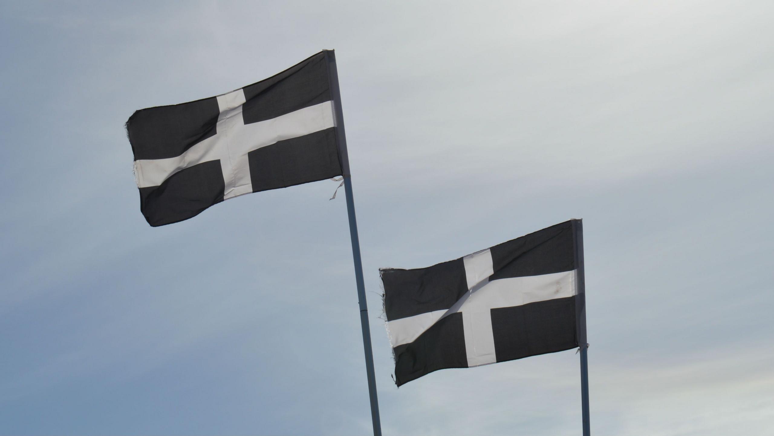 Two Cornwall flags - a white cross on a black background - wave in the air