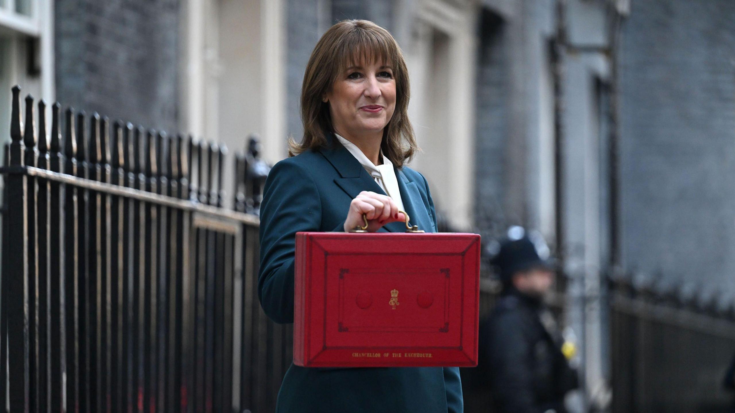 Chancellor of the Exchequer Rachel Reeves outside 11 Downing Street on Budget Day. She is holding a red box, has brown hair and is wearing a blue suit.