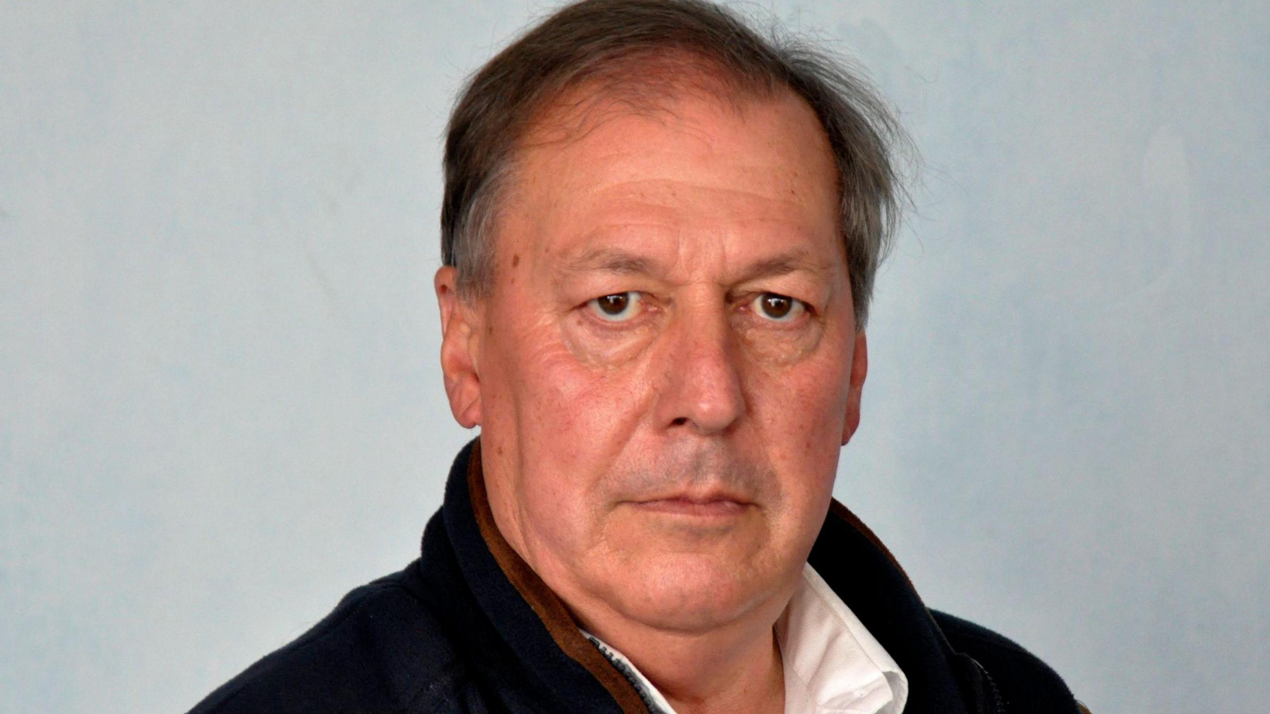 Councillor Steve Davenport pictured from the shoulders up against a plain grey background. He is wearing a white shirt and dark jacket, with . 