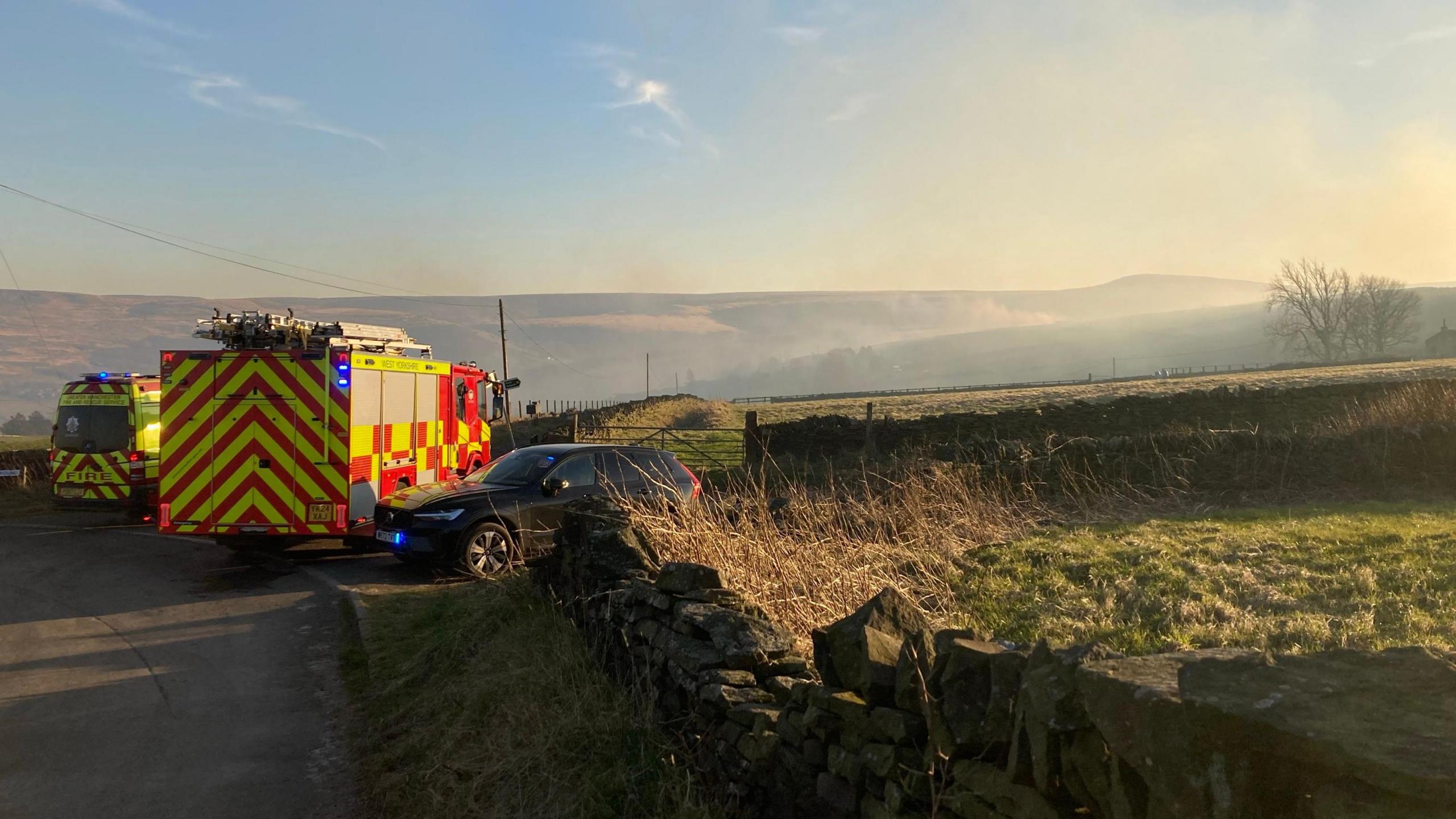 Fire service vehicles with smoke from fire visible in background