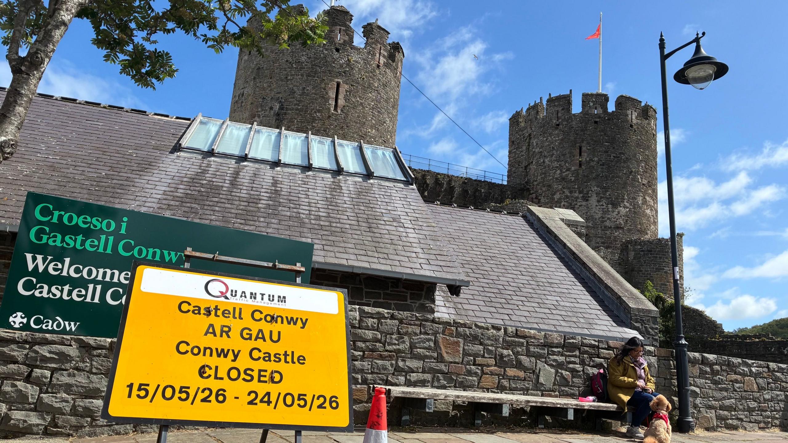 Castell Conwy yn y cefndir ac arwydd melyn yn son fod y castell ar gau rhwng 15 Mai a 24 Mai. 