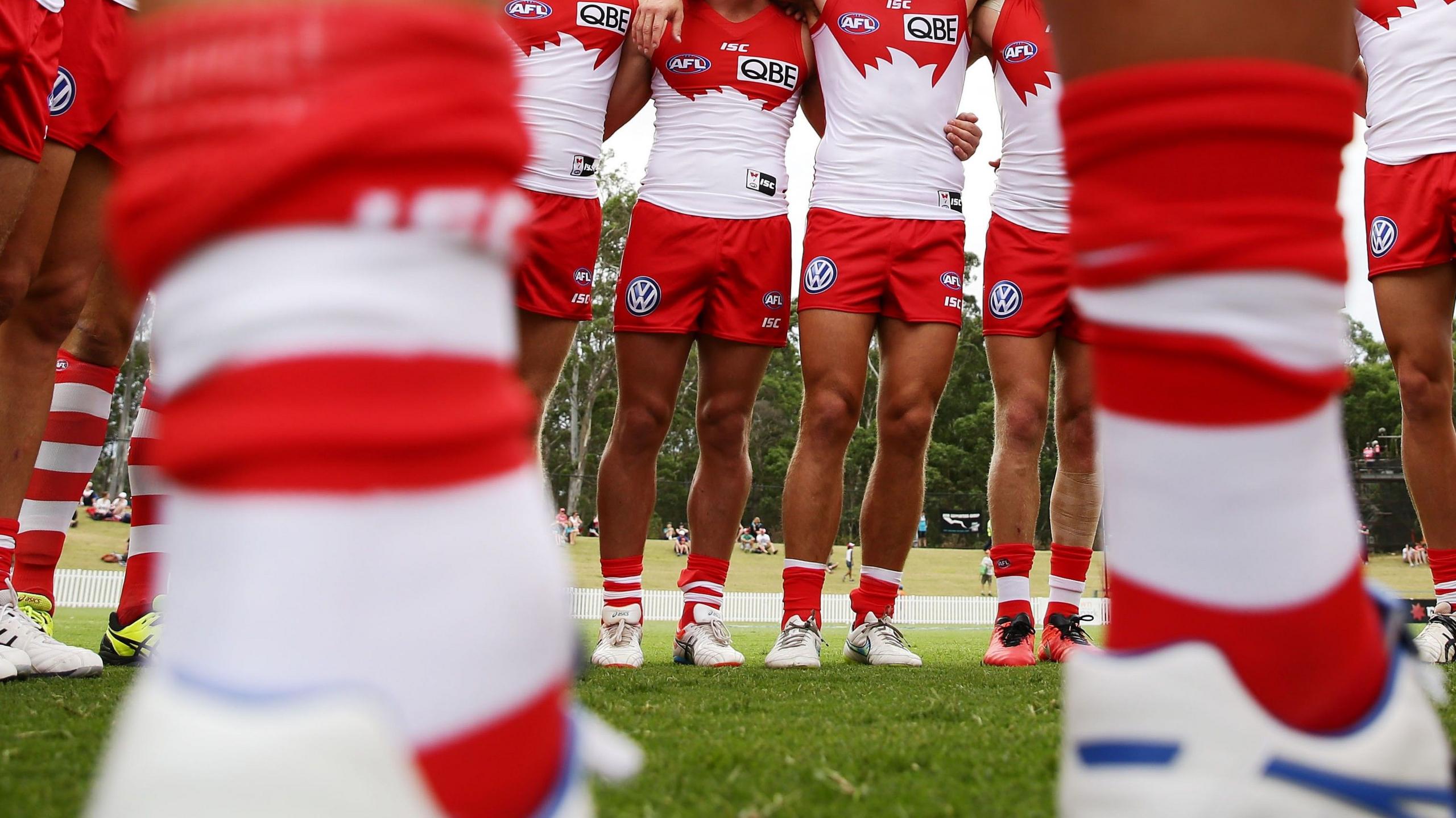 A pair of blurry legs in the foreground with a line of Sydney Swans players in the background