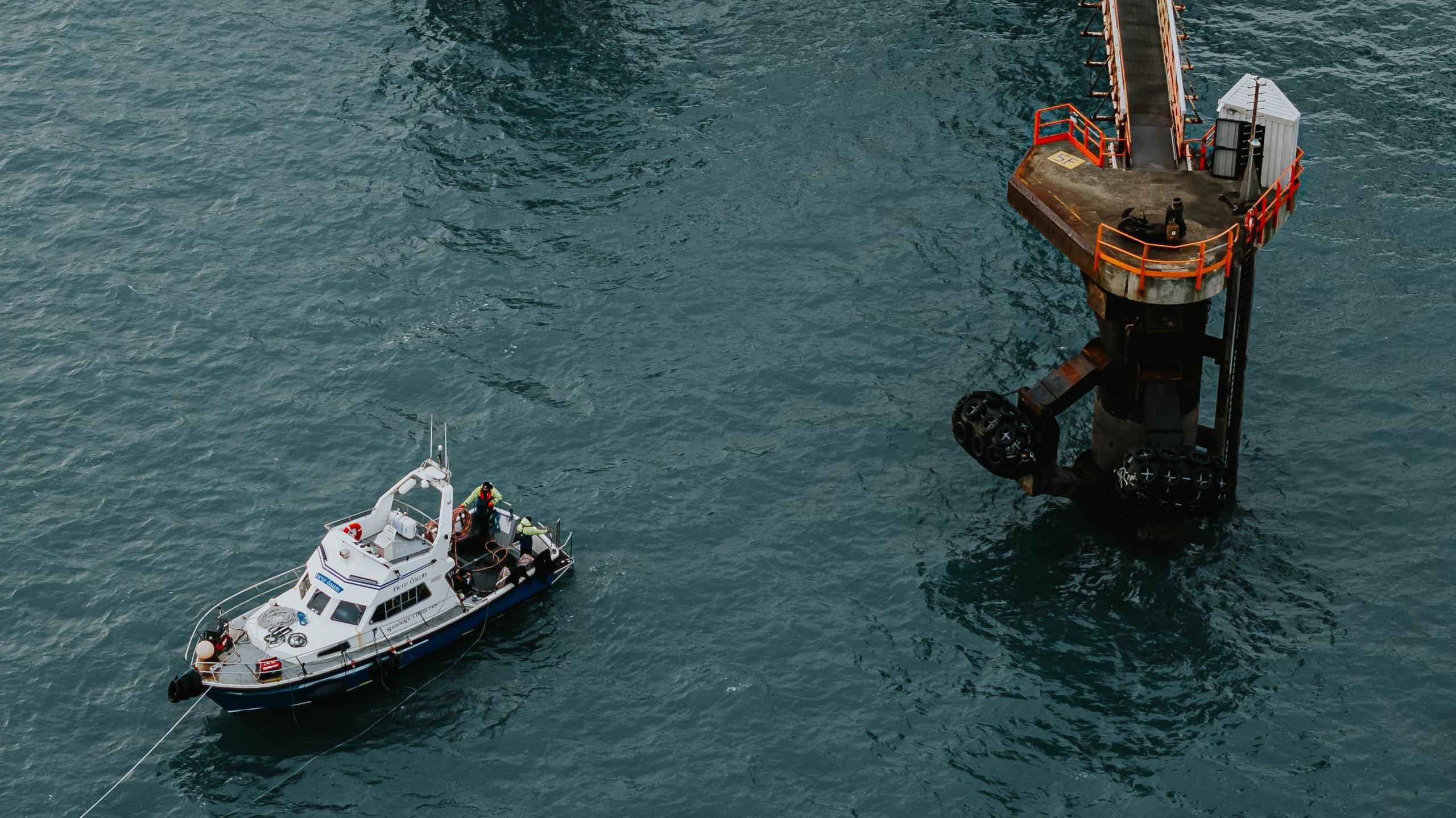 A boat with people working to fix the port. A tower is visible jutting out of the sea.