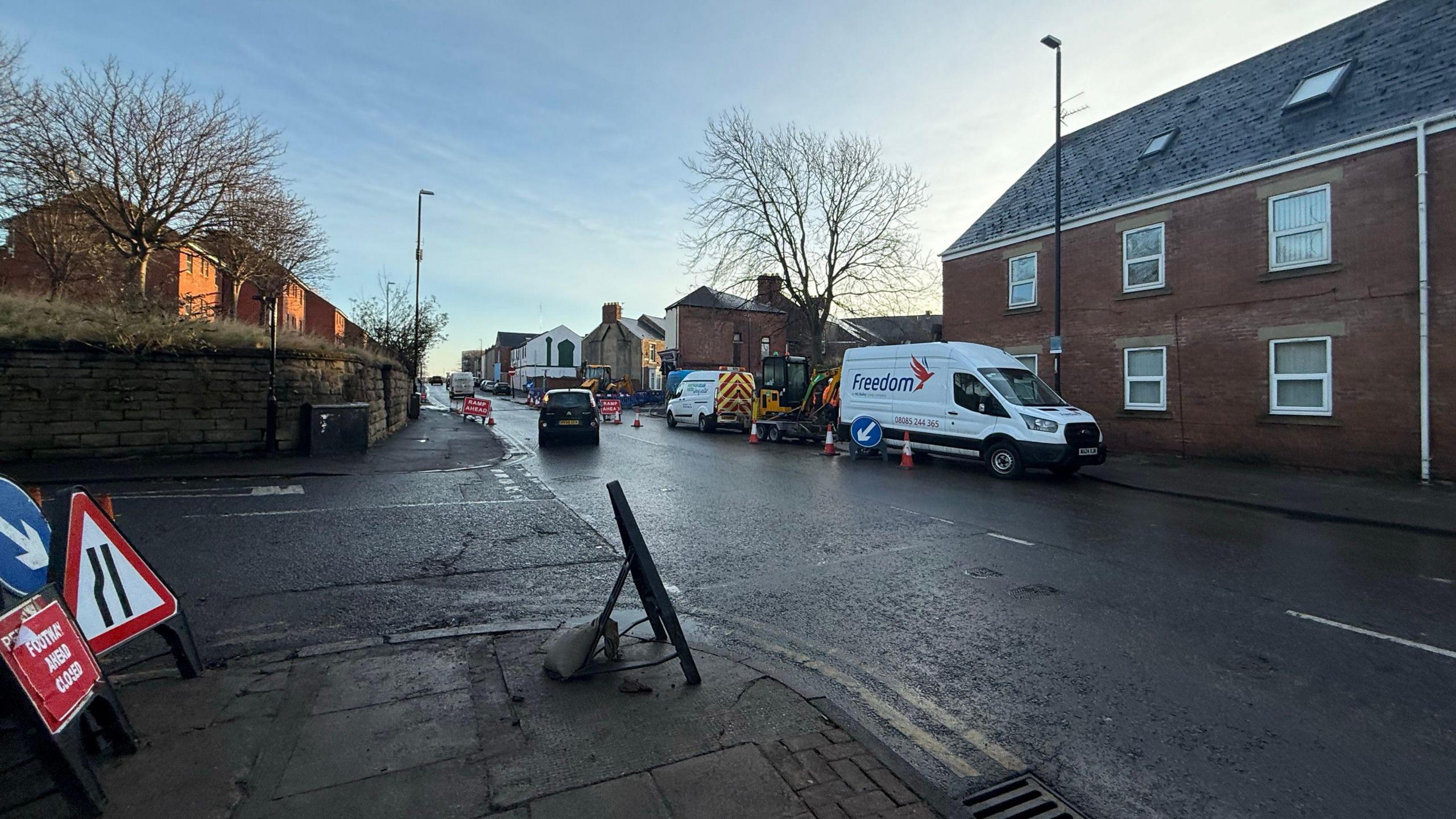 Road with vans on it. It is a clear blue sky. Roadwork signs are on the road. 