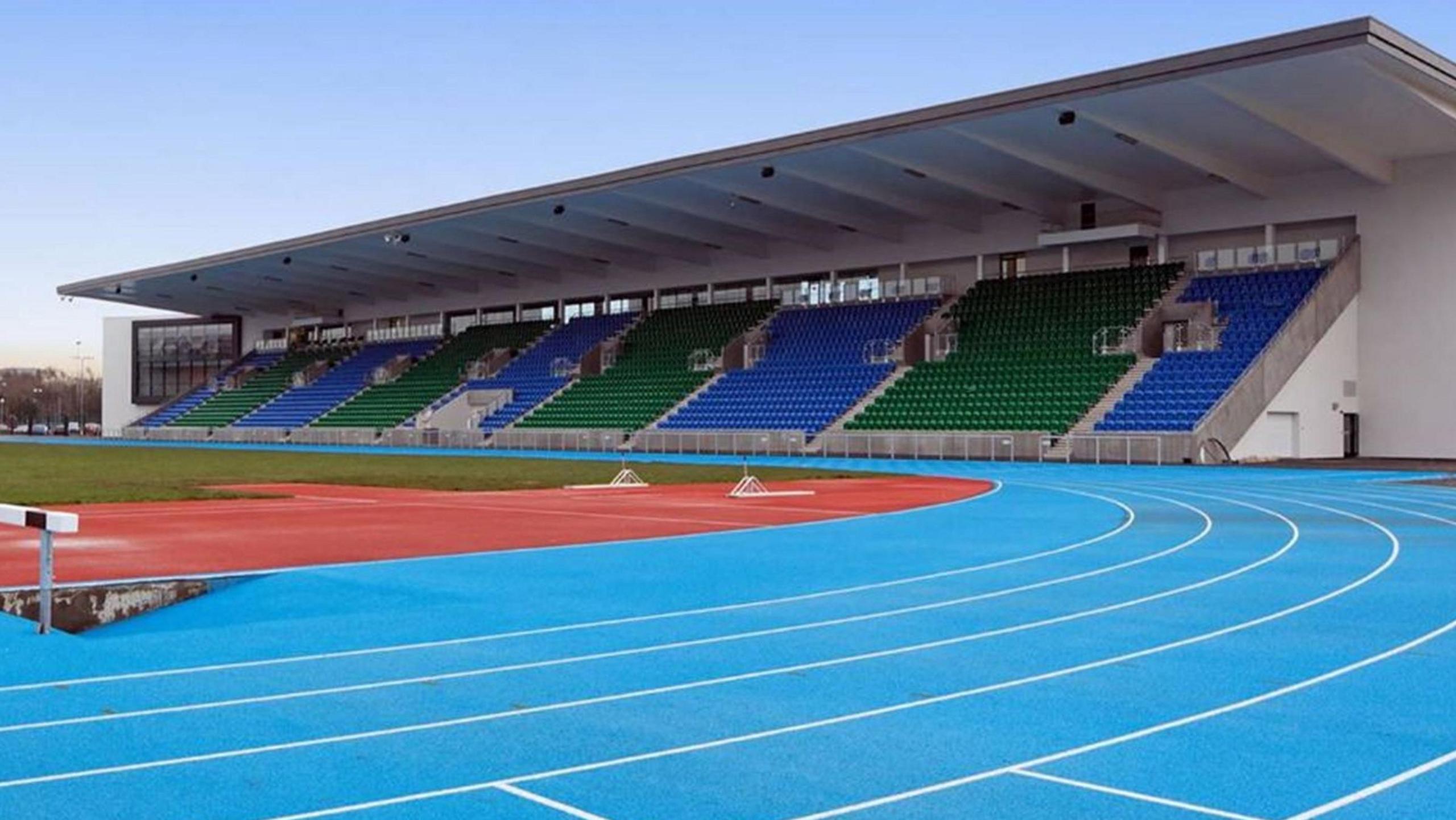 Blue running track at Scotstoun stadium, with blue and green stands pictured in the background