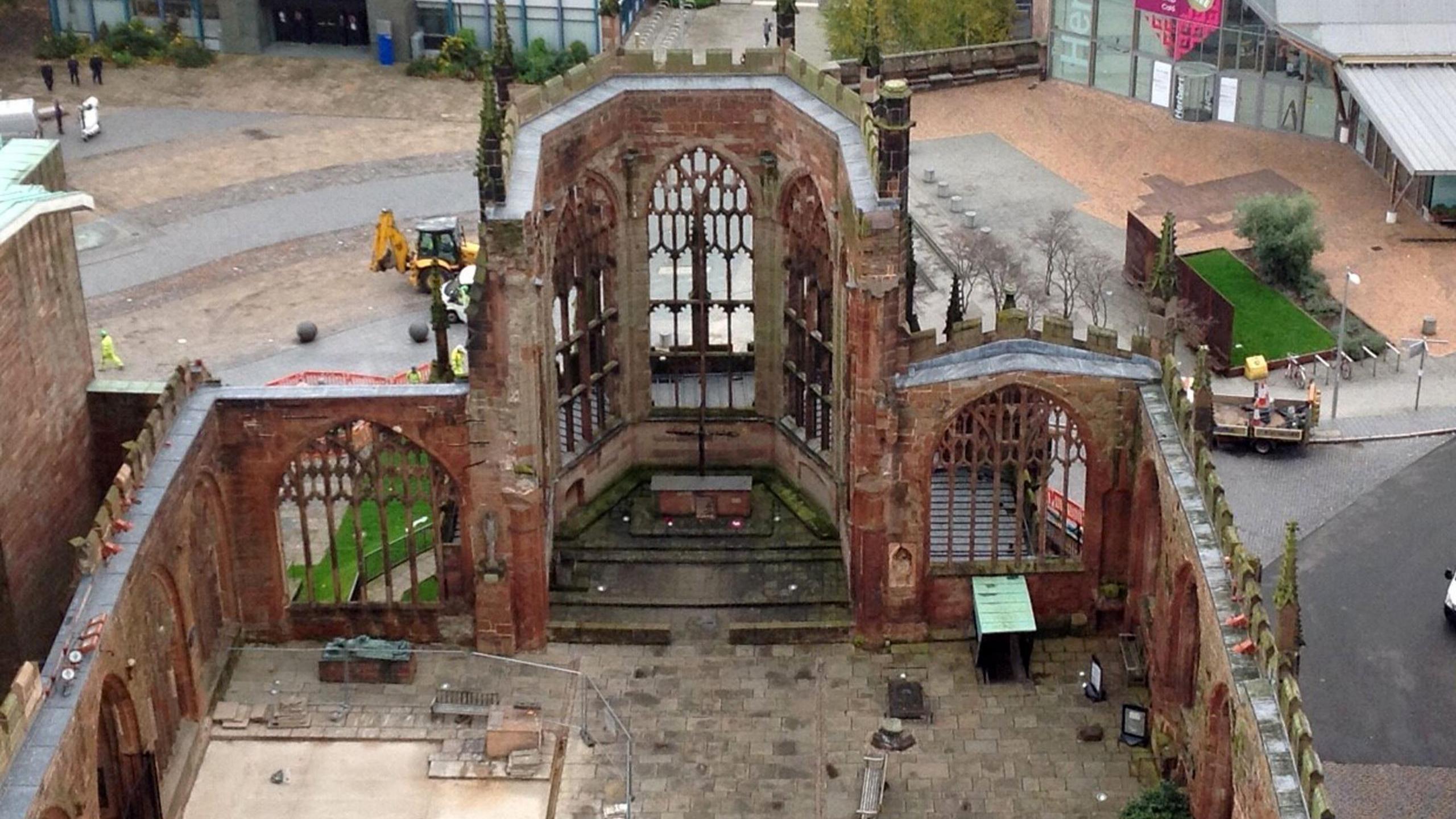 An aerial view of the ruins of Coventry's medieval cathedral. Most of the walls are intact as the camera looks down into the centre of the empty building which has no roof.