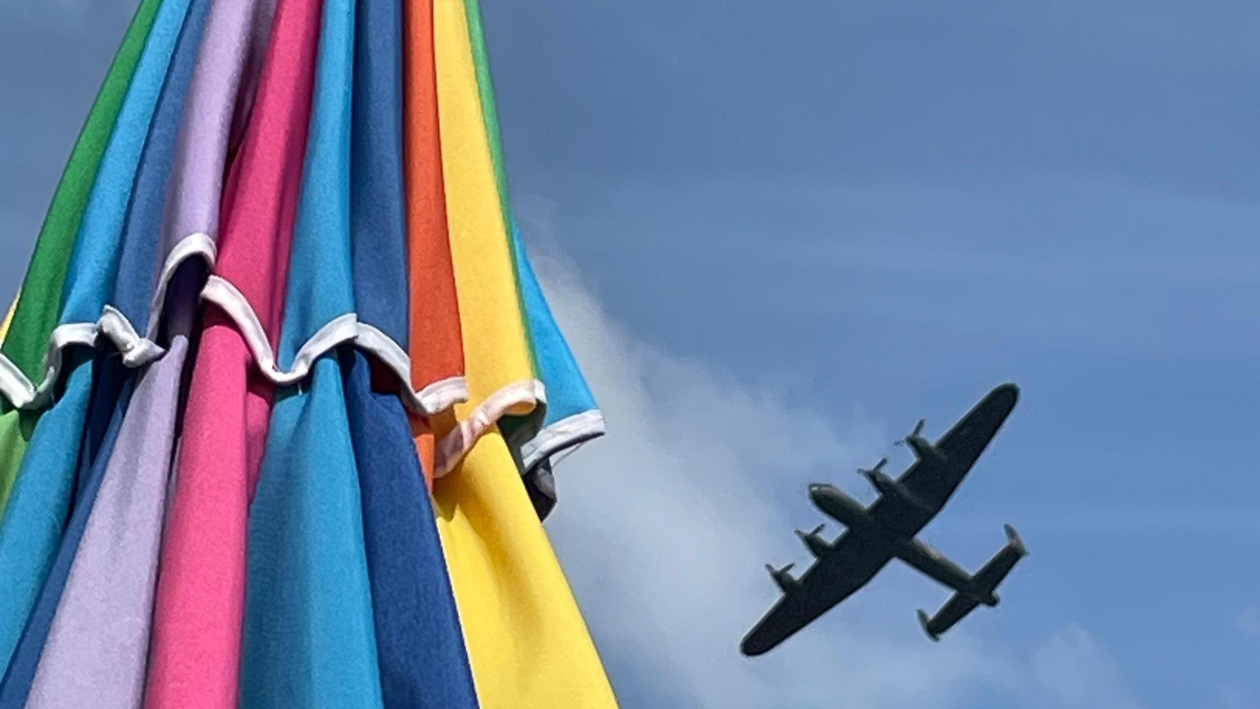 A multi-coloured parasol can be seen on the left-hand side of the photo with a bright blue sky from above showing on the other side. In the sky is an aircraft presumably part of the Bournemouth Air Festival last week.