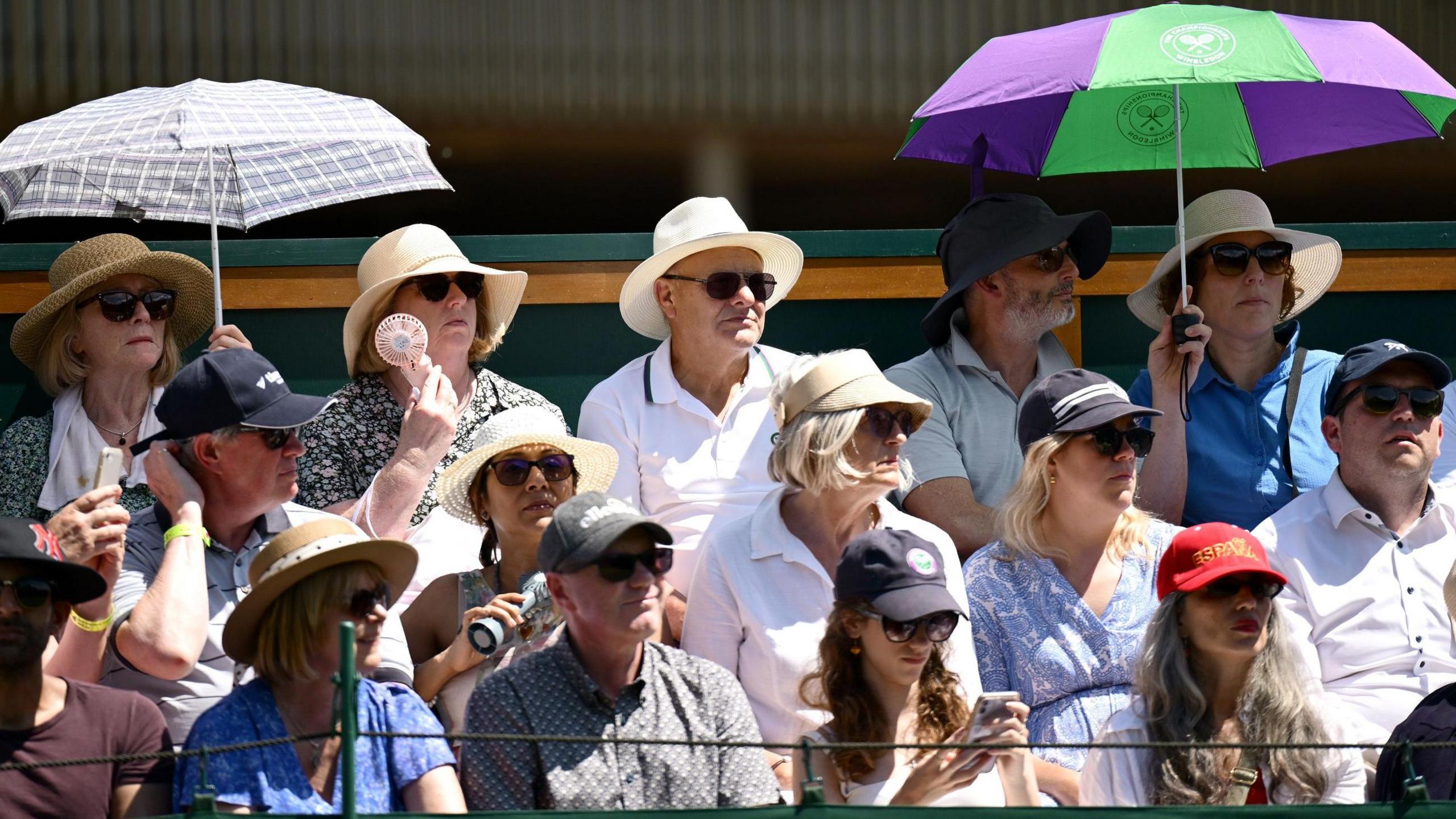 Spectators shade themselves from the sun with umbrellas as they watch the action at Wimbledon