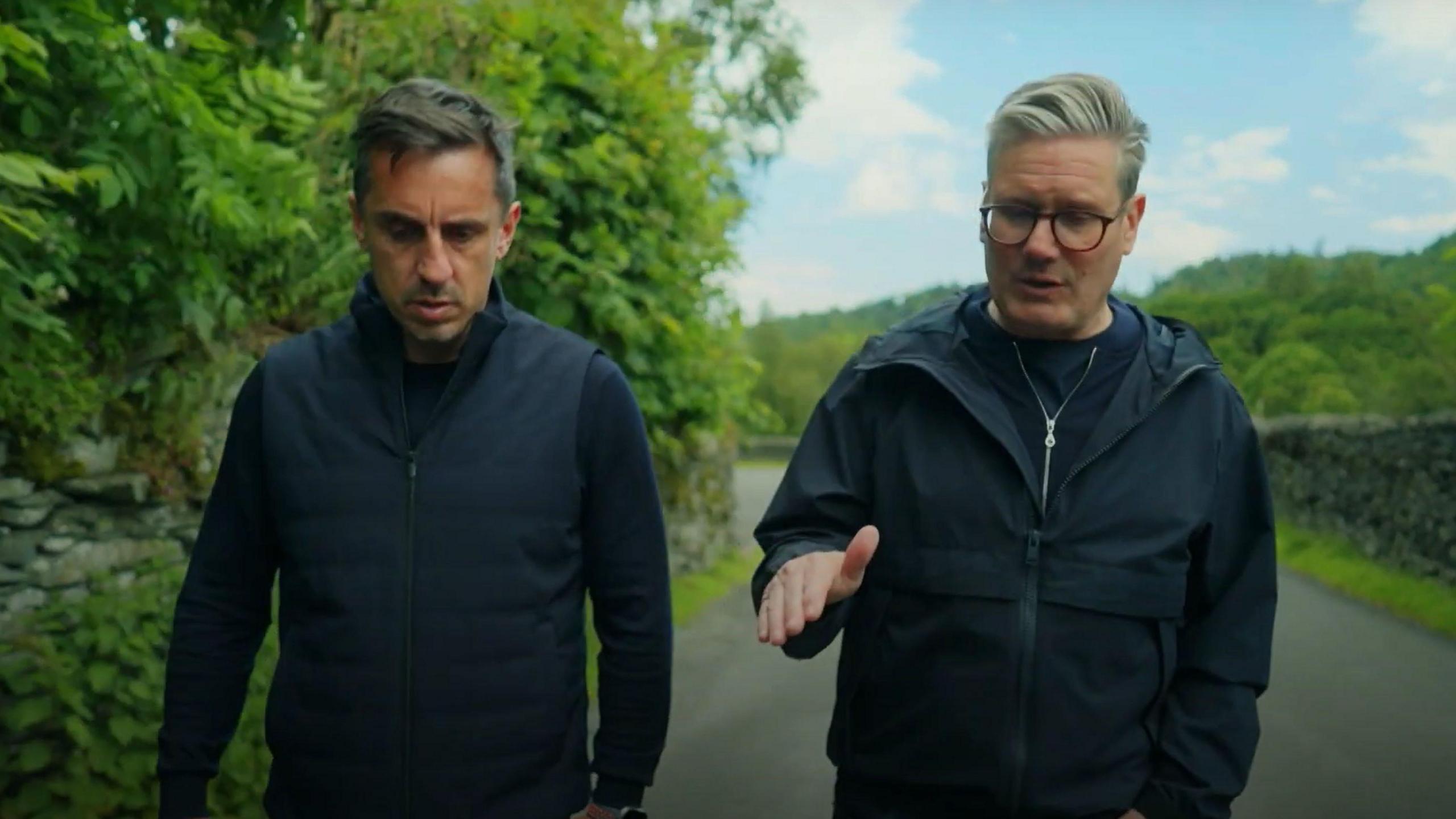 Gary Neville and Sir Keir Starmer walking down a rural road.