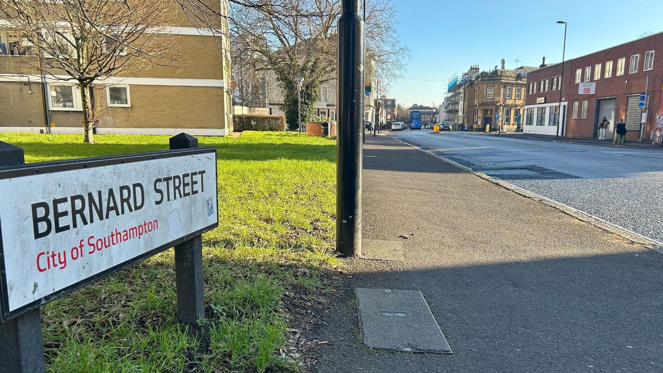 Bernard Street in Southampton with a street sign and lampost in the foreground and the street leading away in the distance with shops and flats.