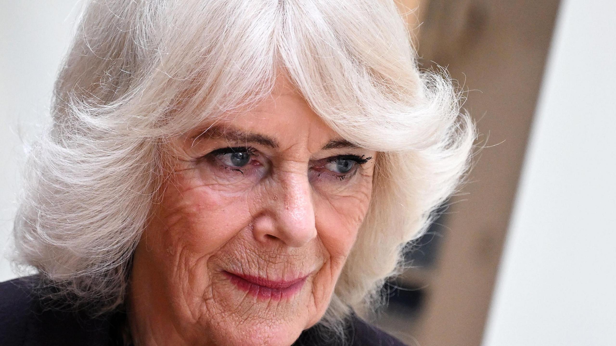 Queen Camilla looking off to right of the camera. She has white hair and is wearing a black jacket.