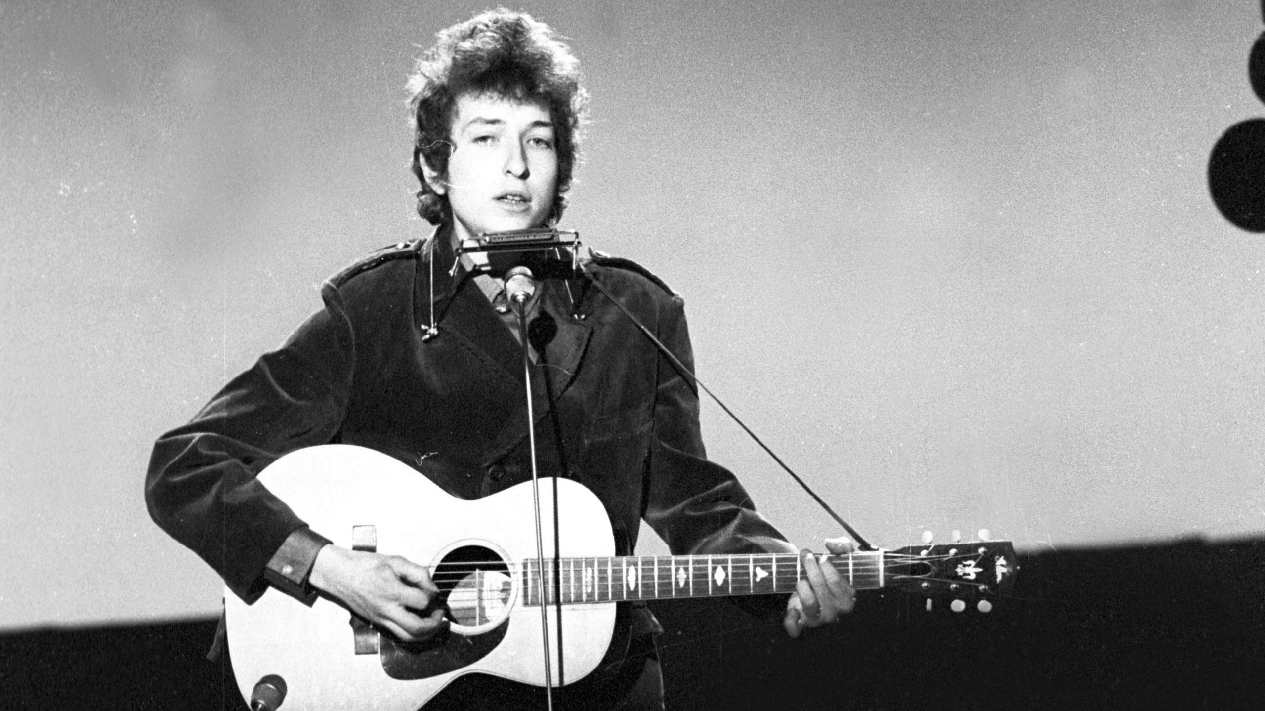 A black and white image of Bob Dylan playing guitar on stage