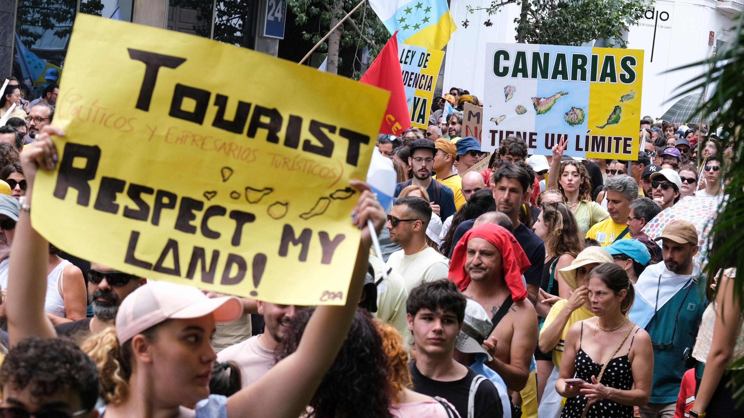 A crowd of people - some holding flags and protest placards - taking part in a protest to demand change to the Canary Islands' tourism