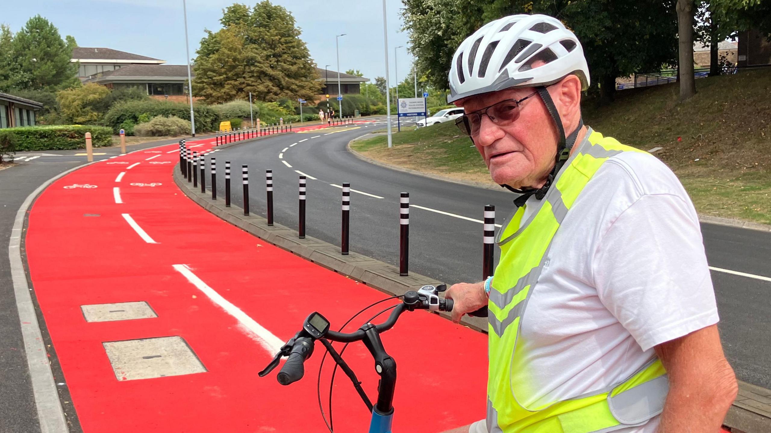 William wearing a white T-shirt and a green high-visibility jacket and a white cycling helmet - sitting on his blue cycle 